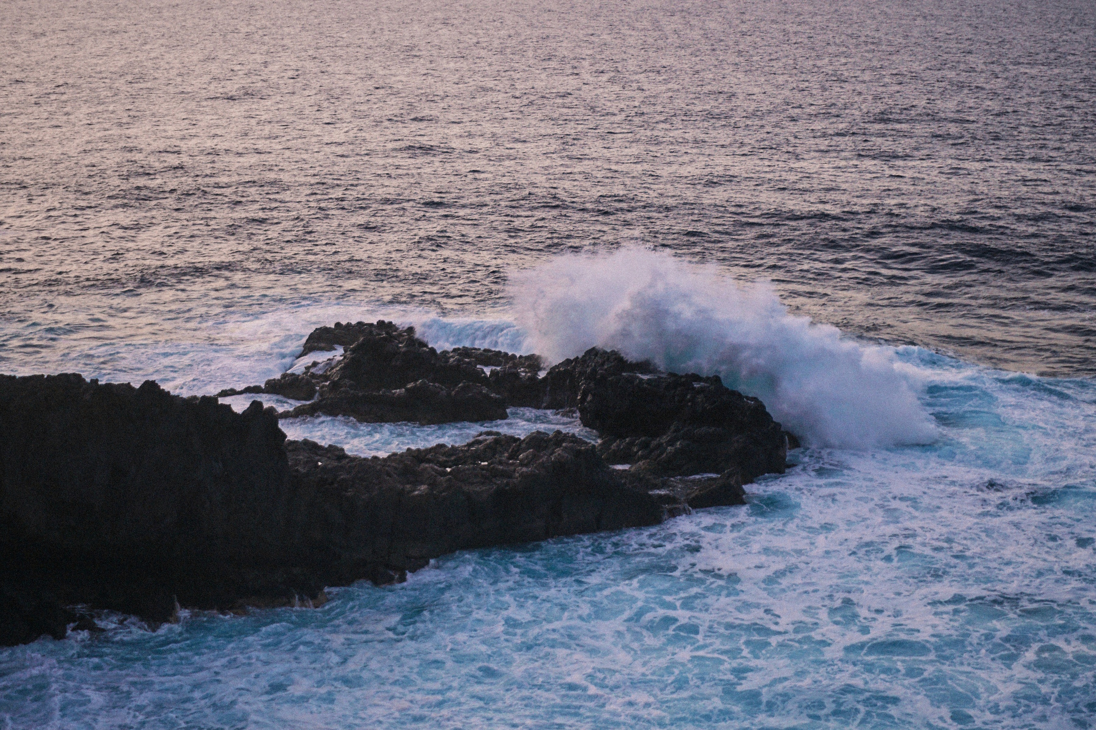 Eine Welle bricht sich an schwarzen Lavafelsen im Abendlicht