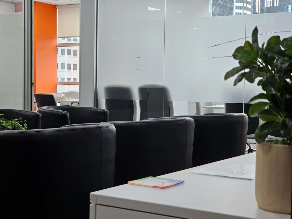 The reception area of a mediation room provider, with a plant in the forehround and two mediation rooms in the background, with seats in the waiting area in view.