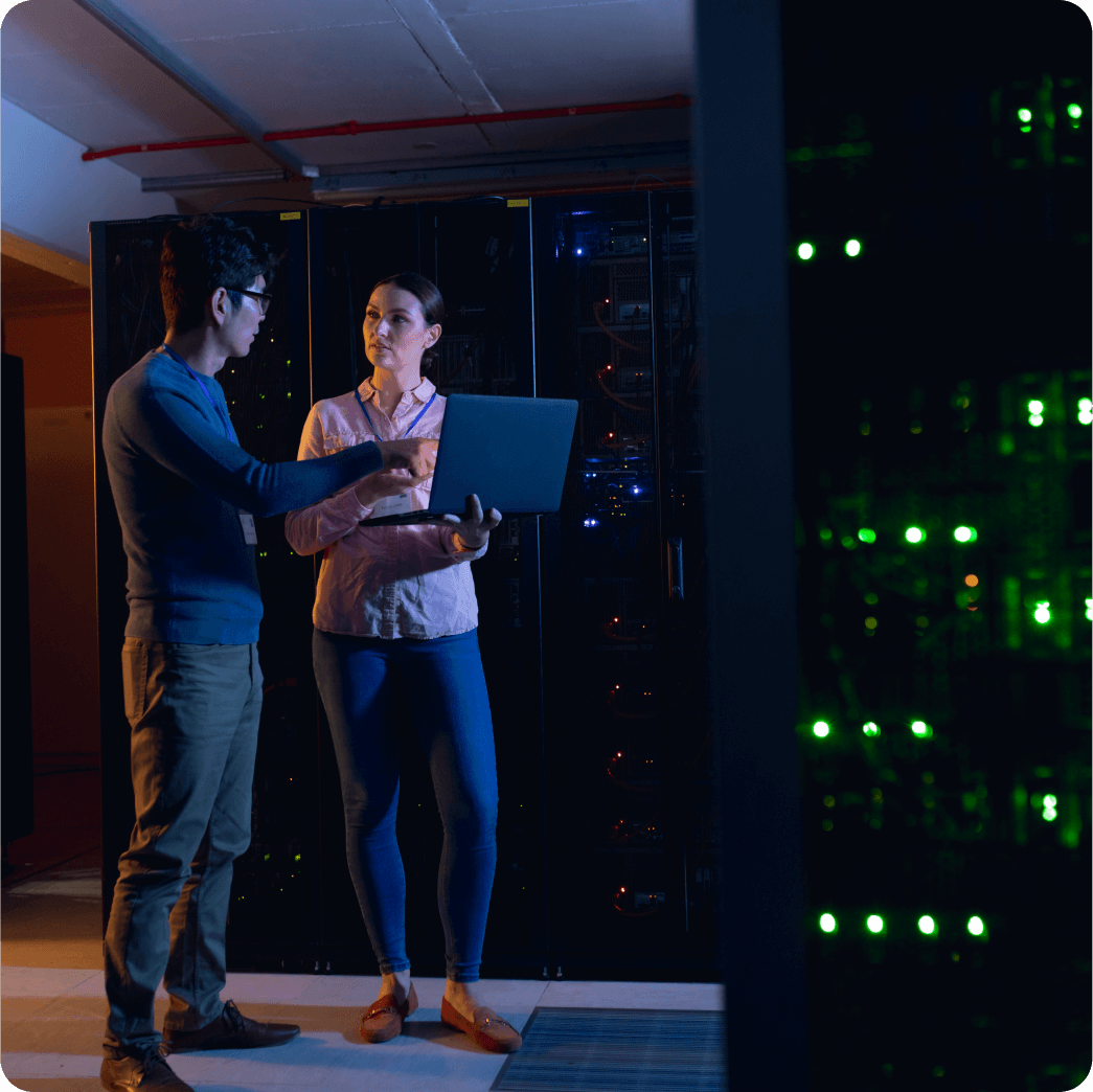 A man wearing blue shirt working on laptop inside server room