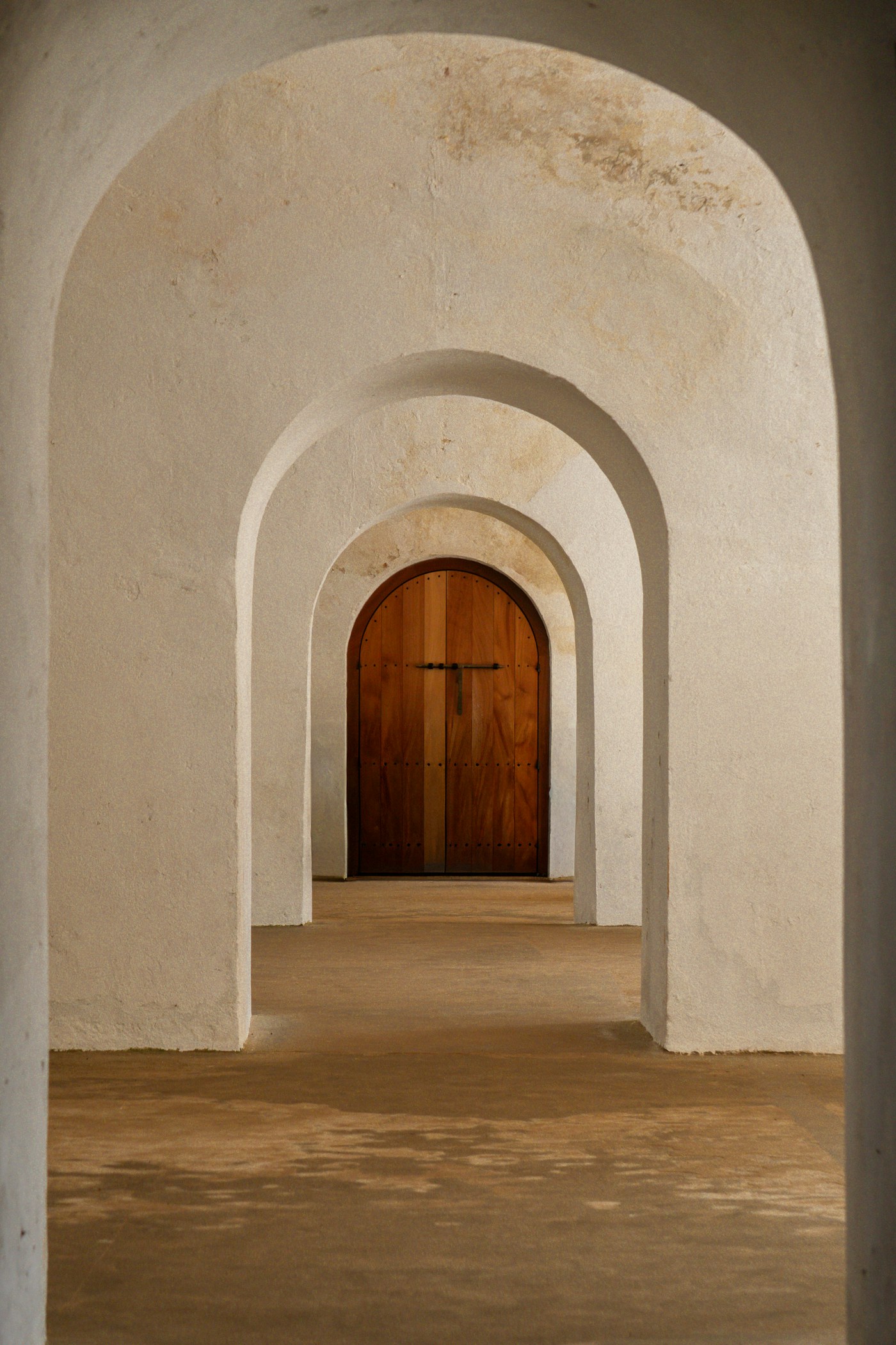 Arched plaster corridor closing on an oak door
