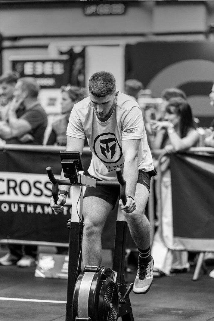 A man with defined abs holding onto a vertical pole in a gym, looking to the side.