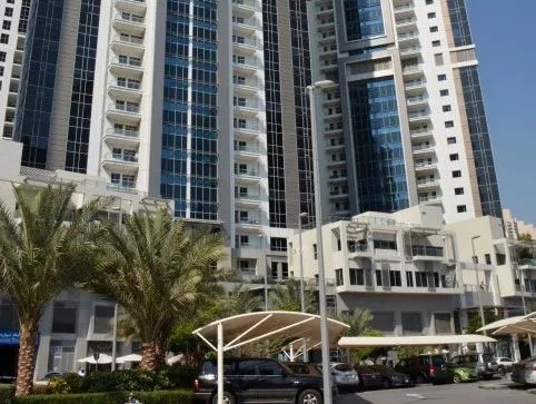 Ground-level perspective highlighting the height of two modern Dubai skyscrapers, with parking in the foreground.