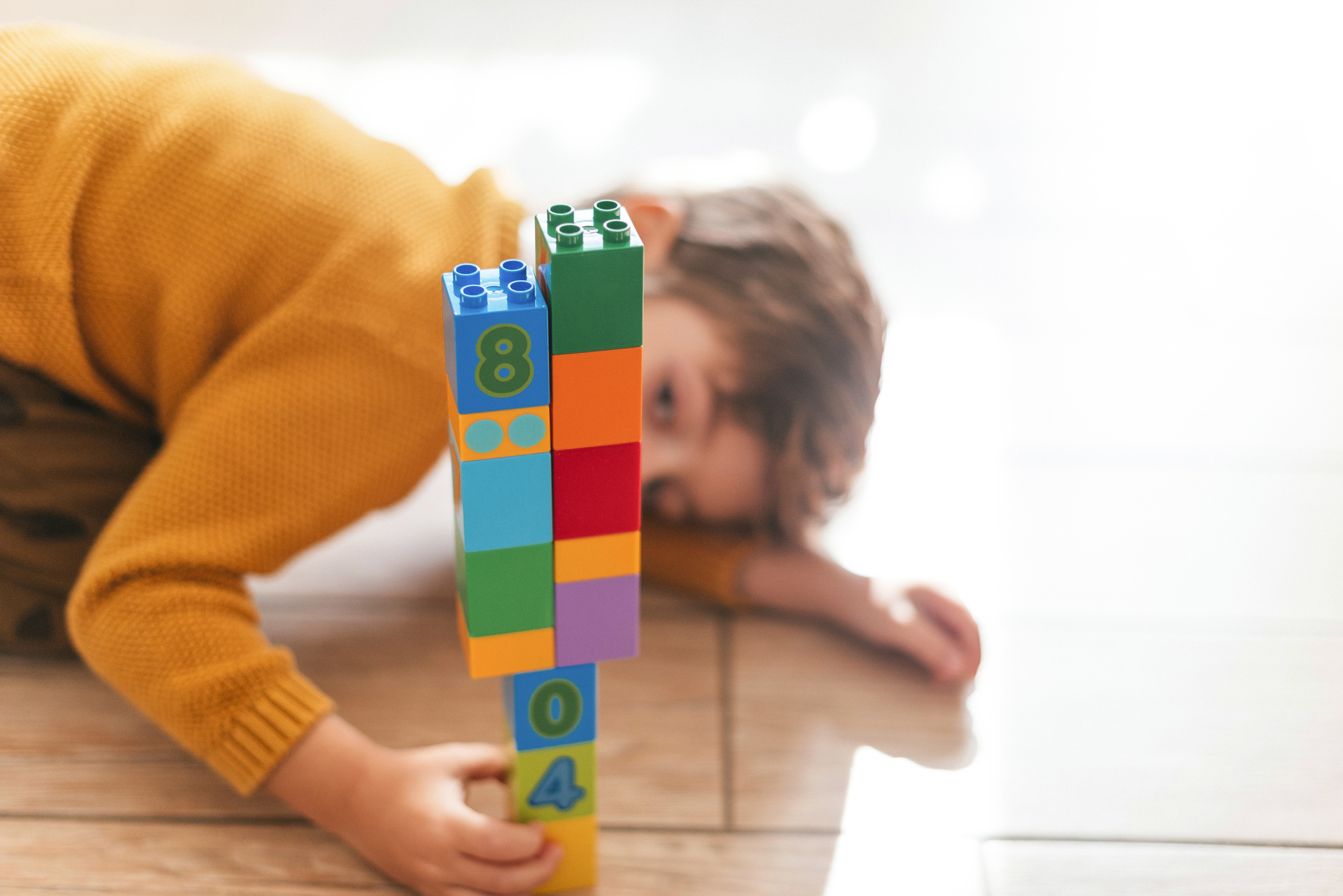 Imagem com um brinquedo, tipo Lego, montado e uma criança desfocada ao fundo