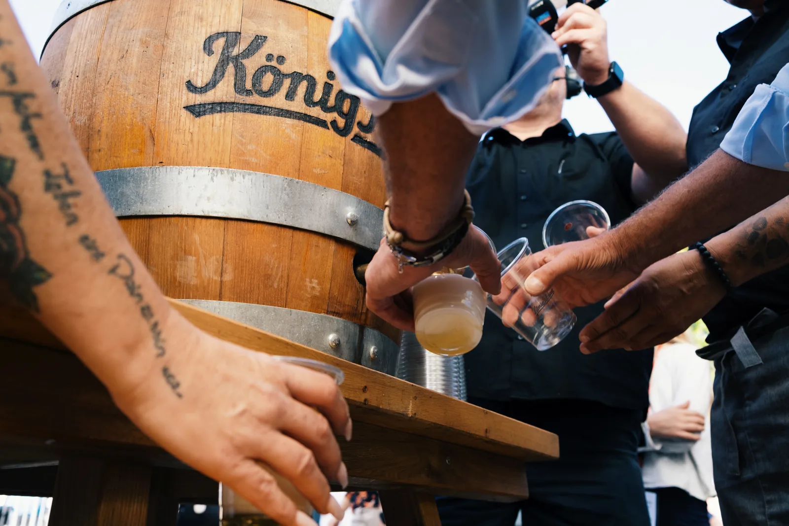 Bier wird am Fass gezapft, mehrere Hände greifen nach den Gläsern.