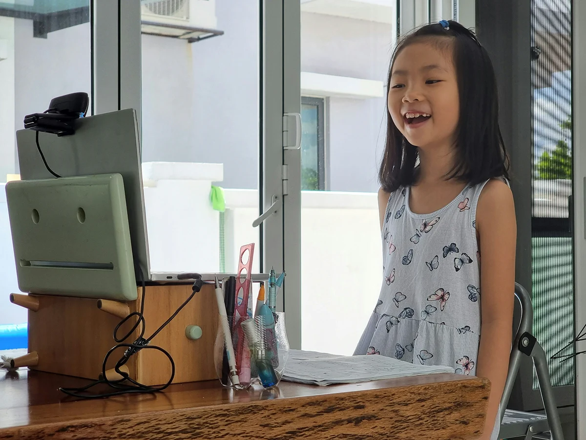 A girl smiling during an online lesson at a laptop.