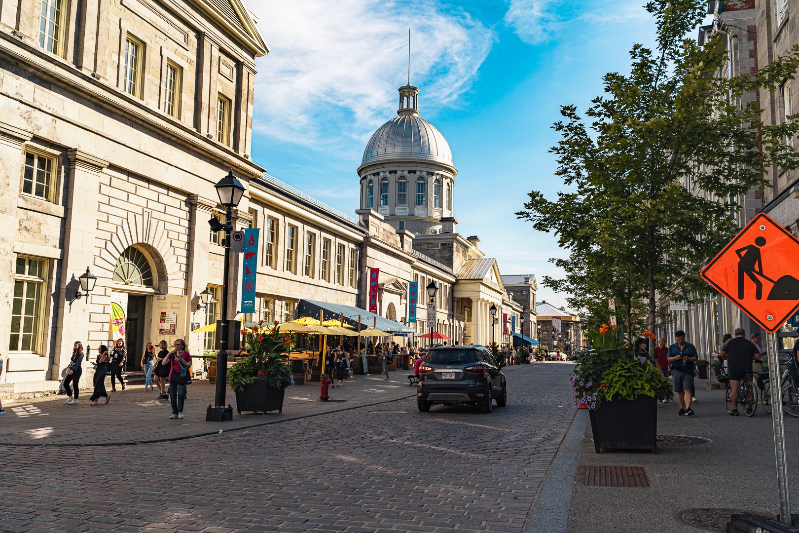 Rue animée du Vieux-Montréal avec le marché Bonsecours en arrière-plan sous un ciel bleu.