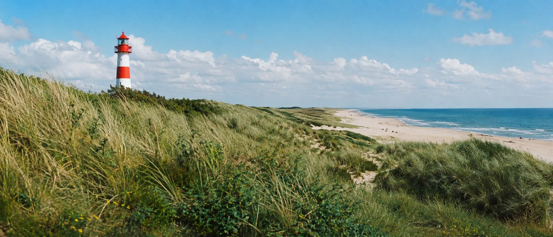 Schleswig-holsteinische Küste mit Dünen, Leuchtturm und blauem Meer bei hellem Tageslicht