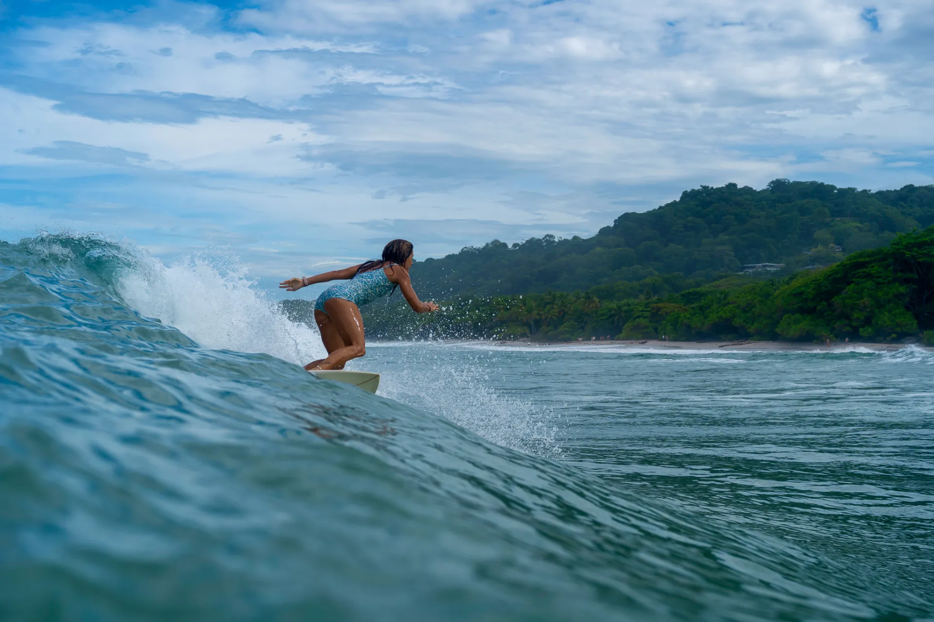 Woman surfing a wave in Santa Teresa, Costa Rica, with the jungle-covered coast behind her