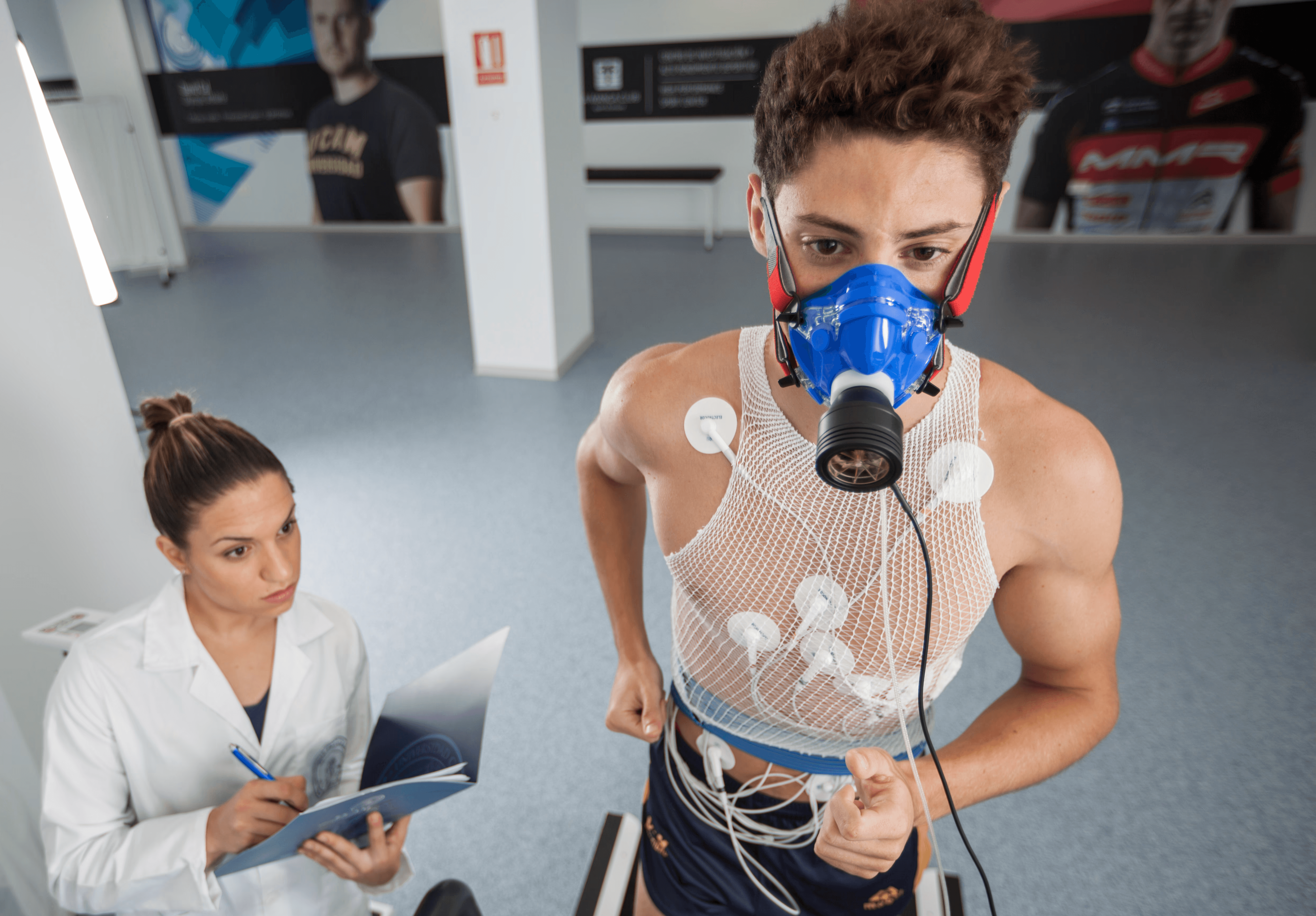 Male athlete undergoing a VO2 max test on a treadmill while wearing a metabolic mask, supervised by a sports scientist taking notes