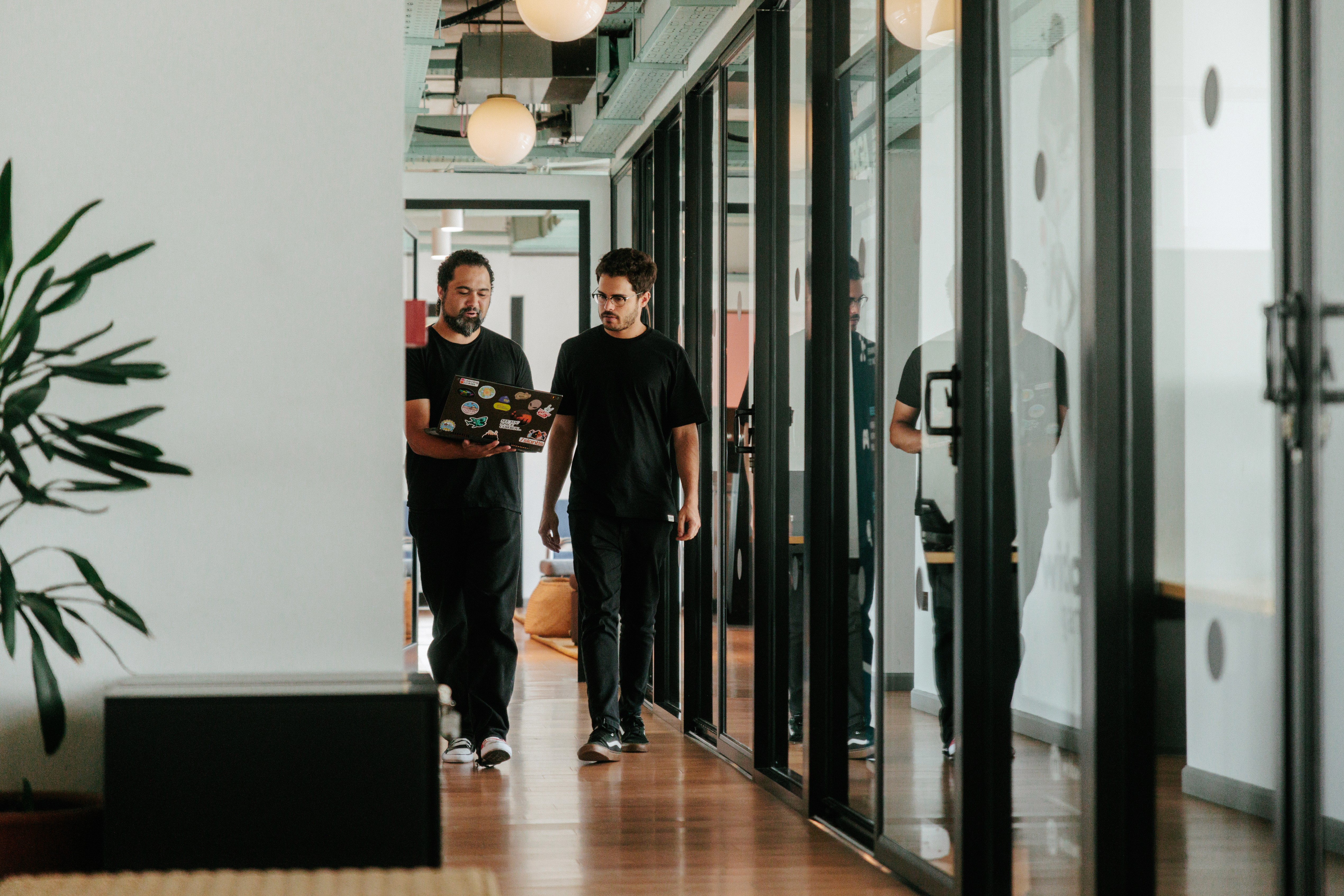 two architects walking through an office corridor looking at a computer together