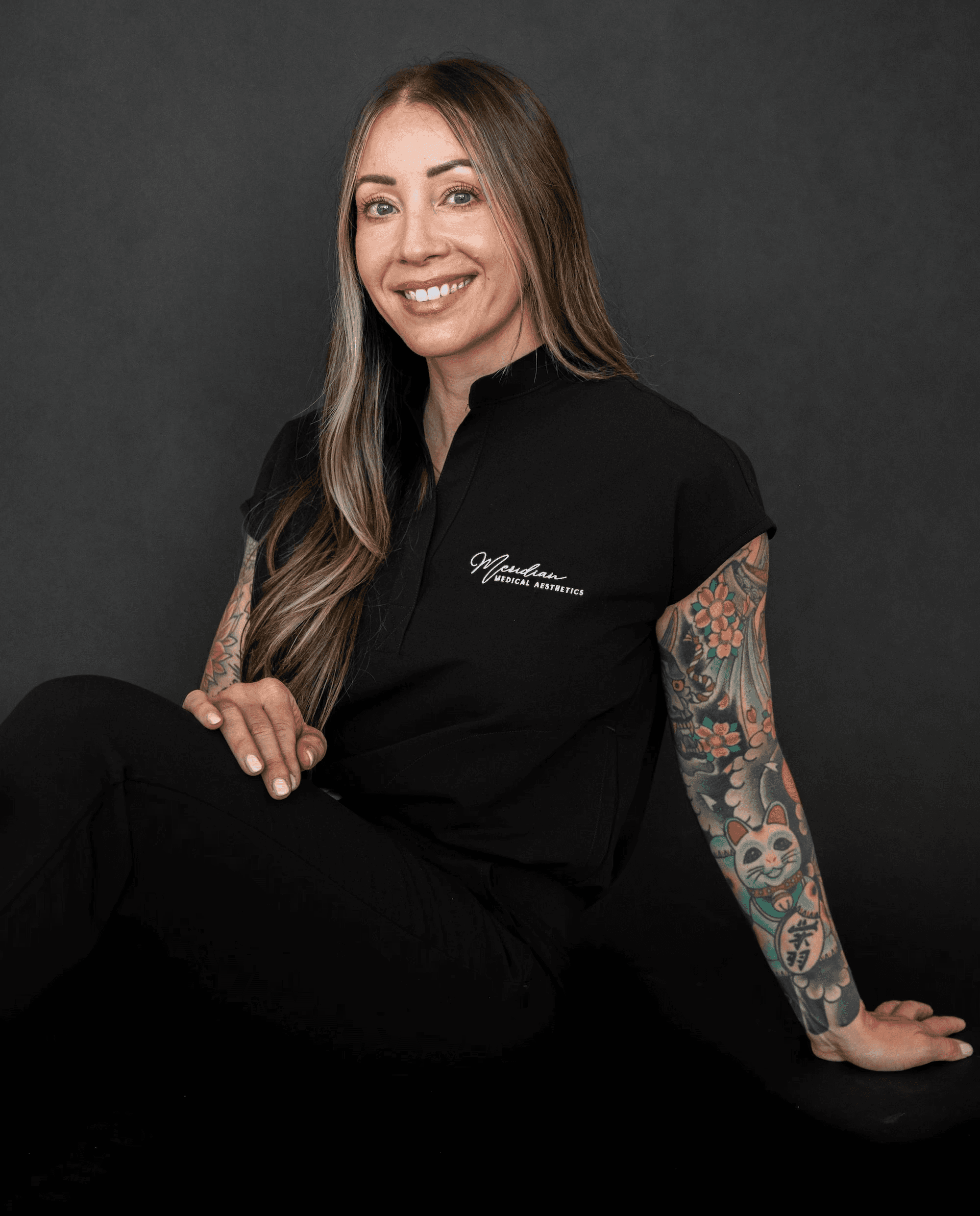 Portrait of licensed esthetician Matsuju Ward of Meridian Medical Aesthetics, smiling in professional uniform against a dark background.