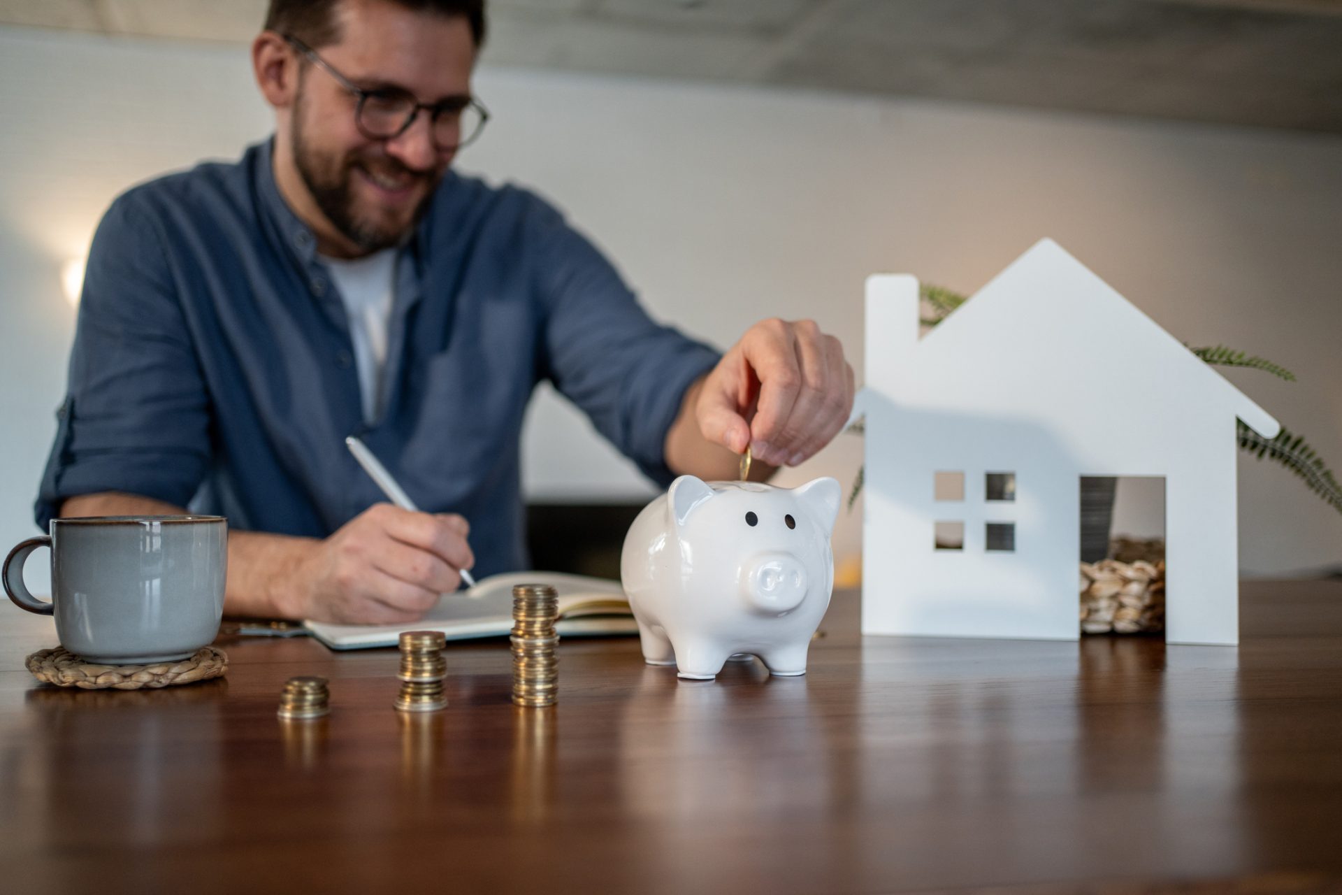 Man saving money in piggy bank near house model