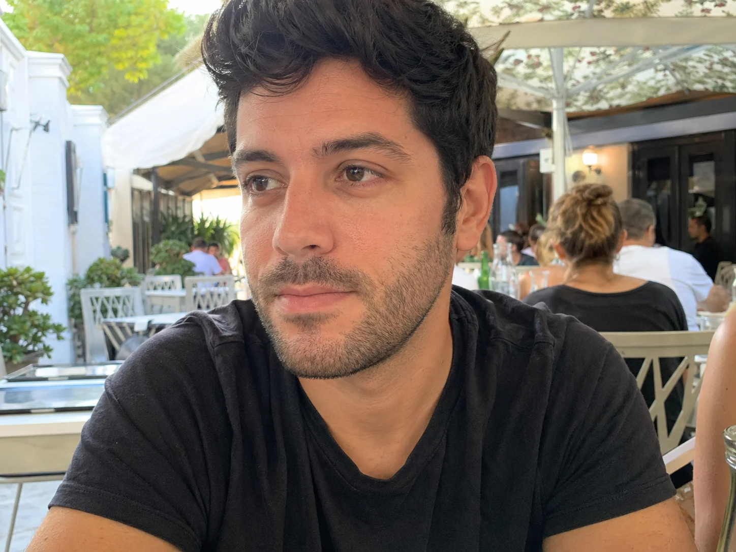 Portrait of a young man sitting at an outdoor café with soft natural daylight and blurred restaurant background