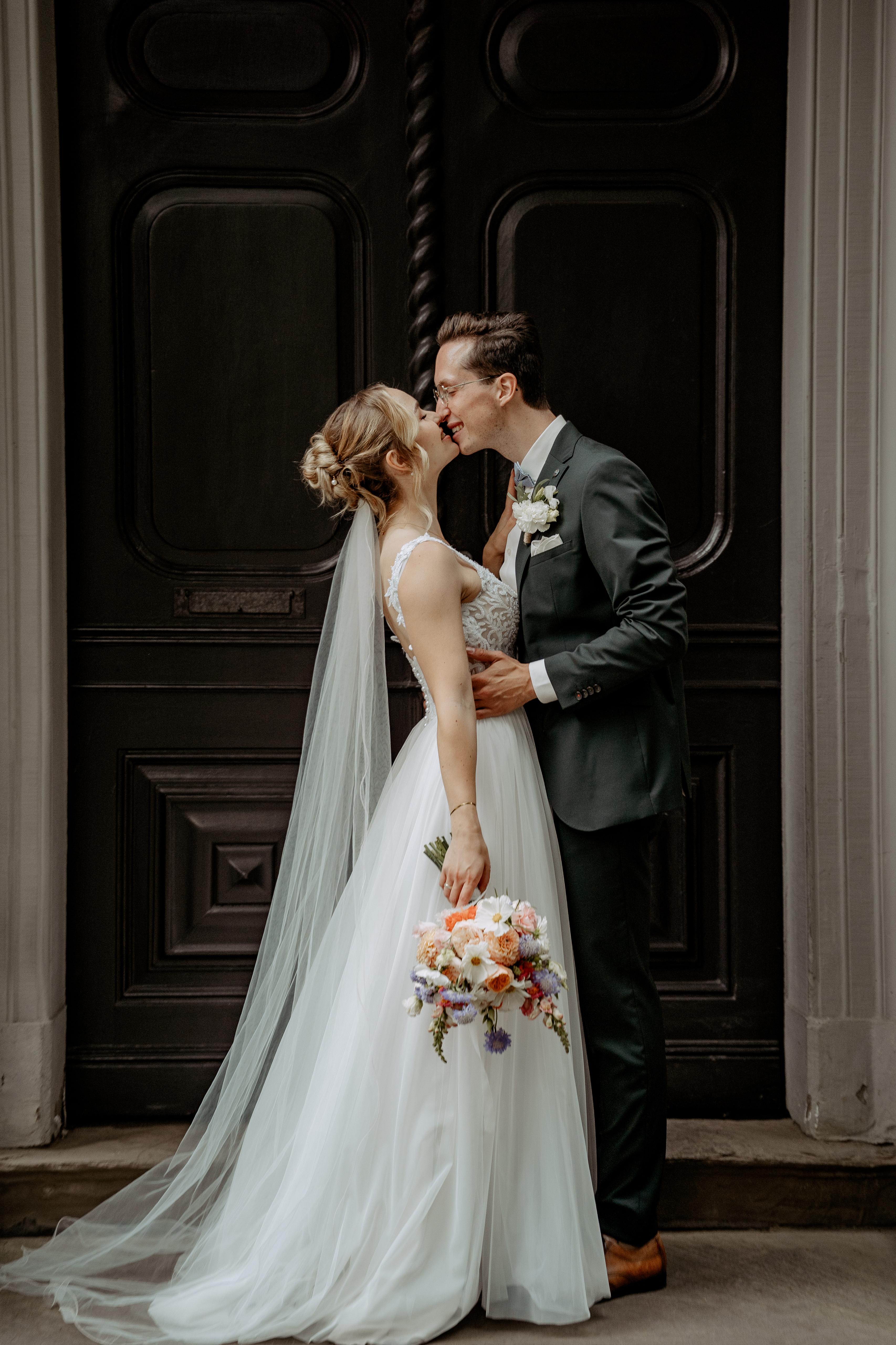 Brautpaar hält sich zärtlich im Arm, Braut trägt weißes Kleid mit Blumenstrauß.