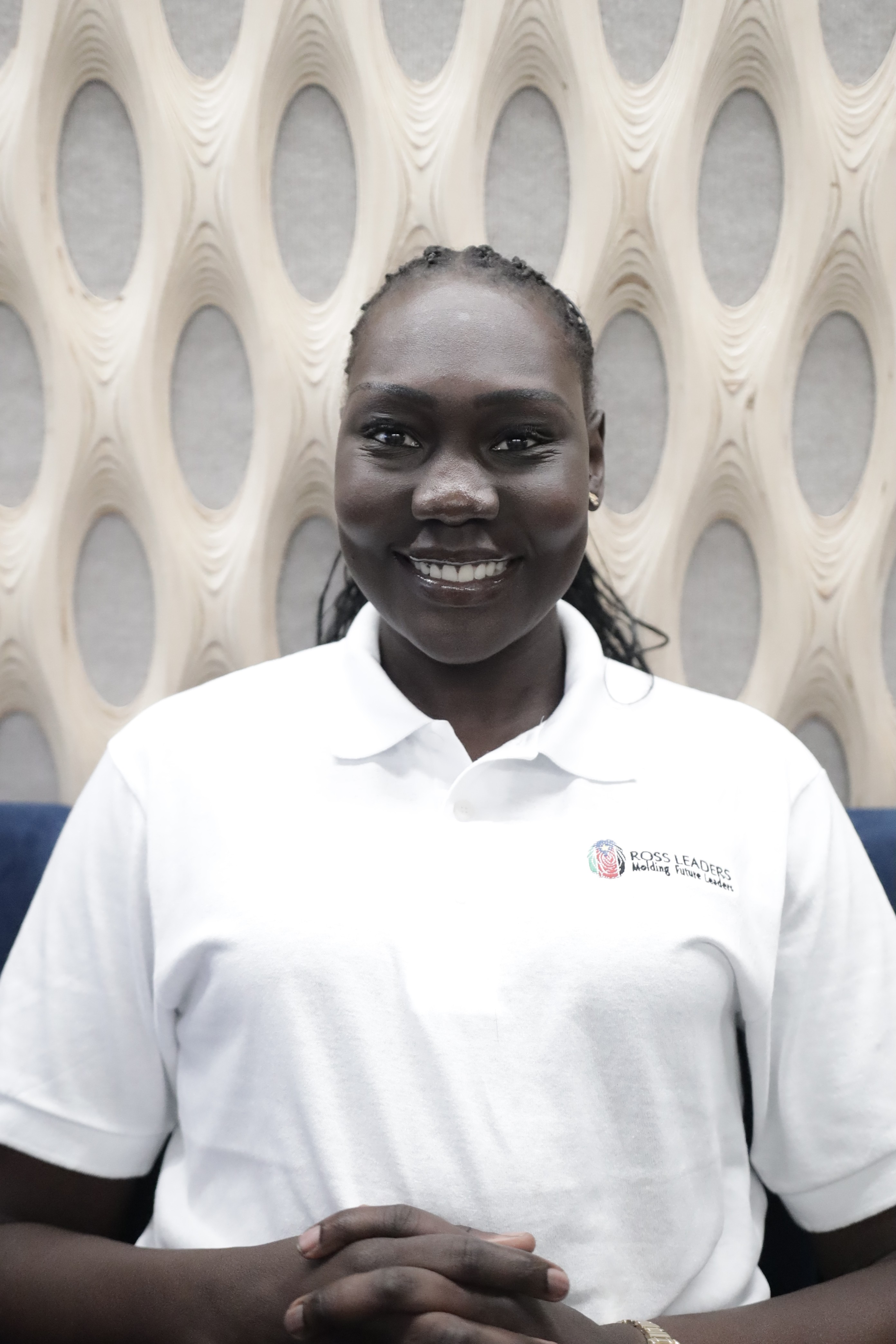 Portrait of a person with red hair, wearing a rust-colored outfit and scarf, set against a neutral gray background.