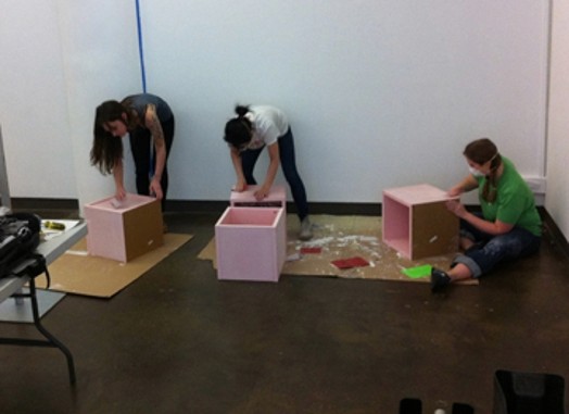three people working on assembling pink boxes