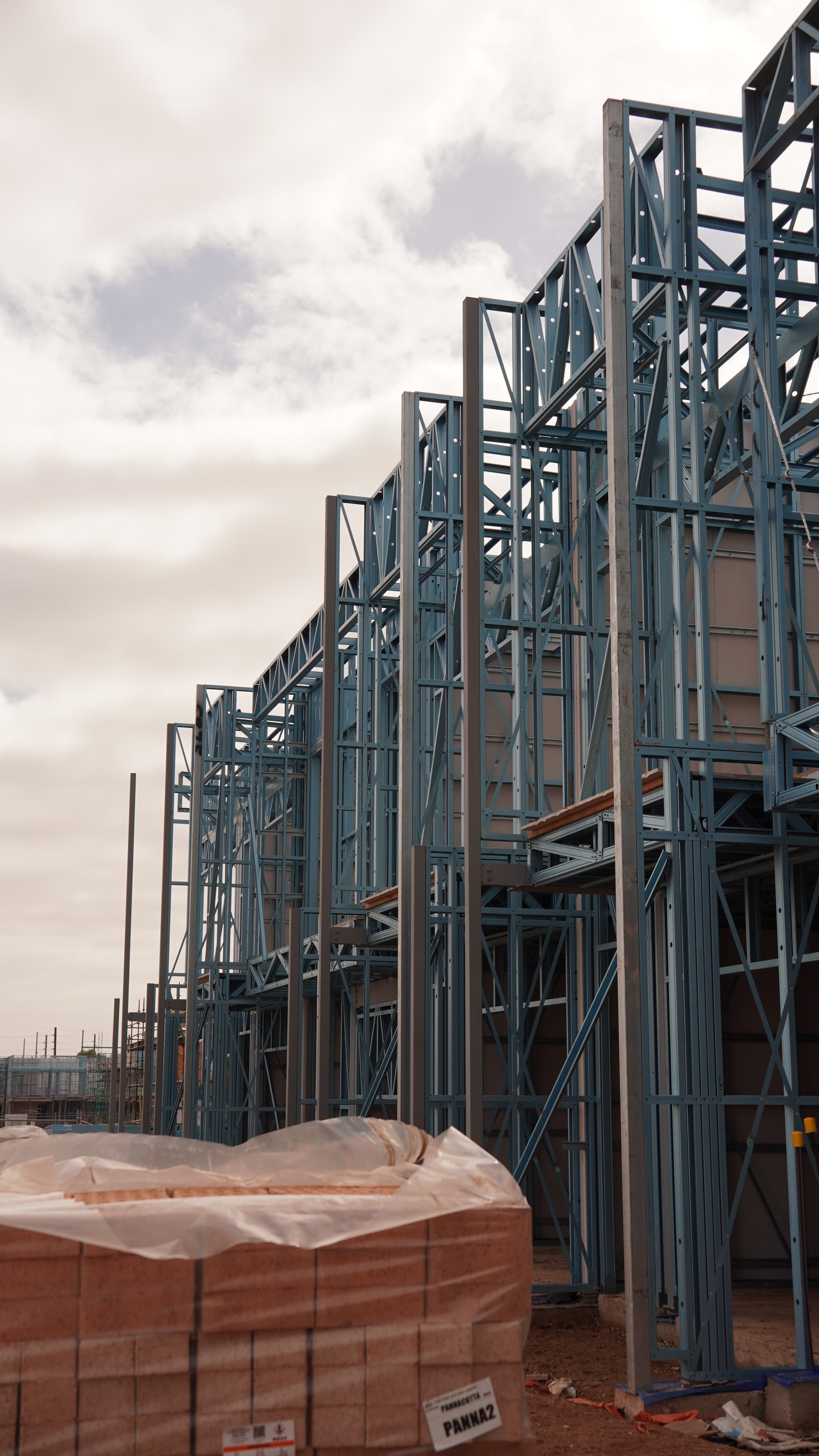 A young person with curly hair smiles at the camera while sitting in front of a laptop against a dark background.