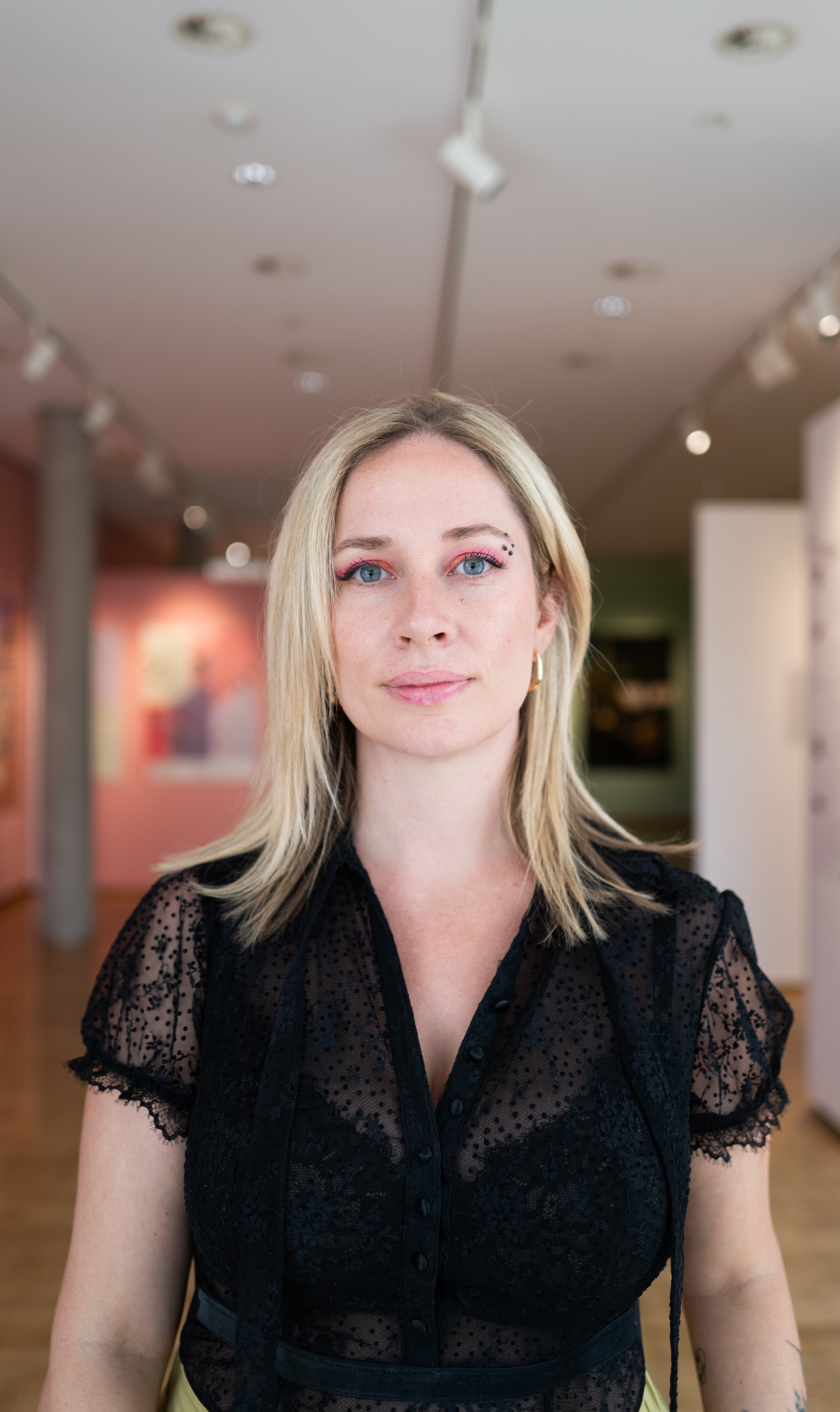 A man with glasses and a beard is looking directly at the camera, seated in a cozy, dimly lit café.