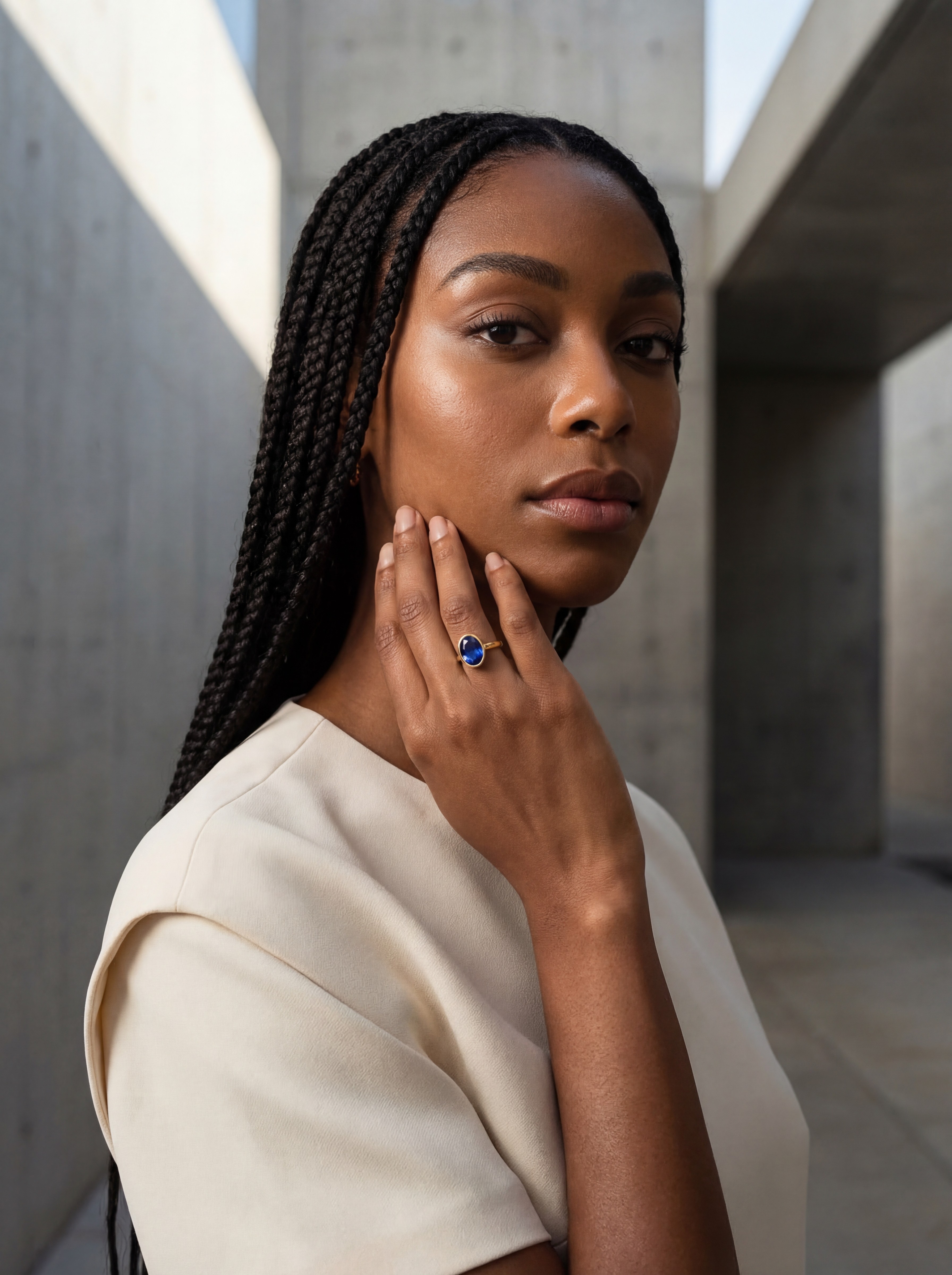 Zaya Amuné AI model wearing sapphire gemstone ring, architectural concrete editorial, elegant cream styling, Gemzy AI jewelry studio