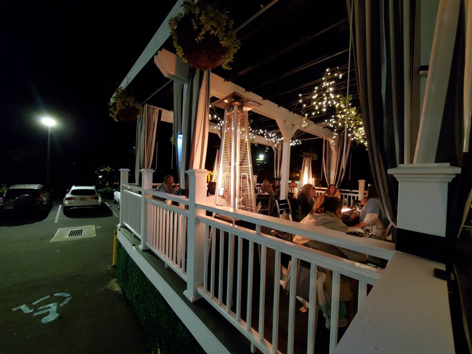 Outdoor dining patio at night, lit by string lights and patio heaters.