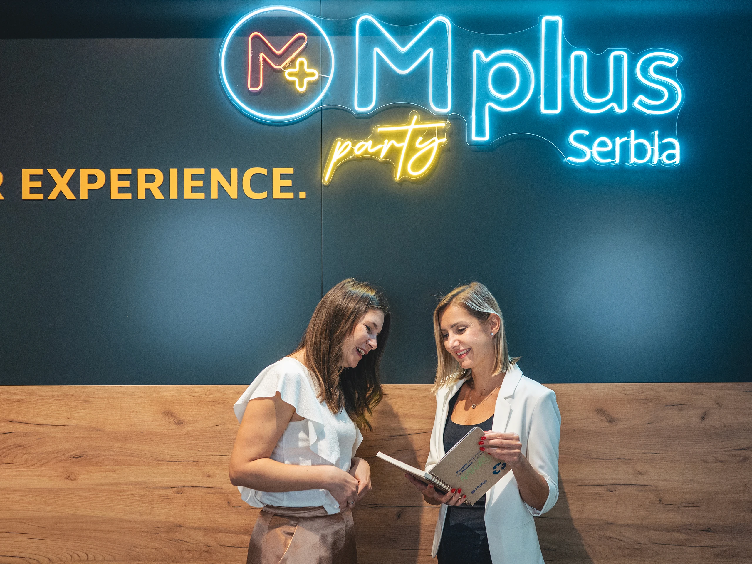 wo colleagues reviewing notes in front of a branded office wall with neon signage.