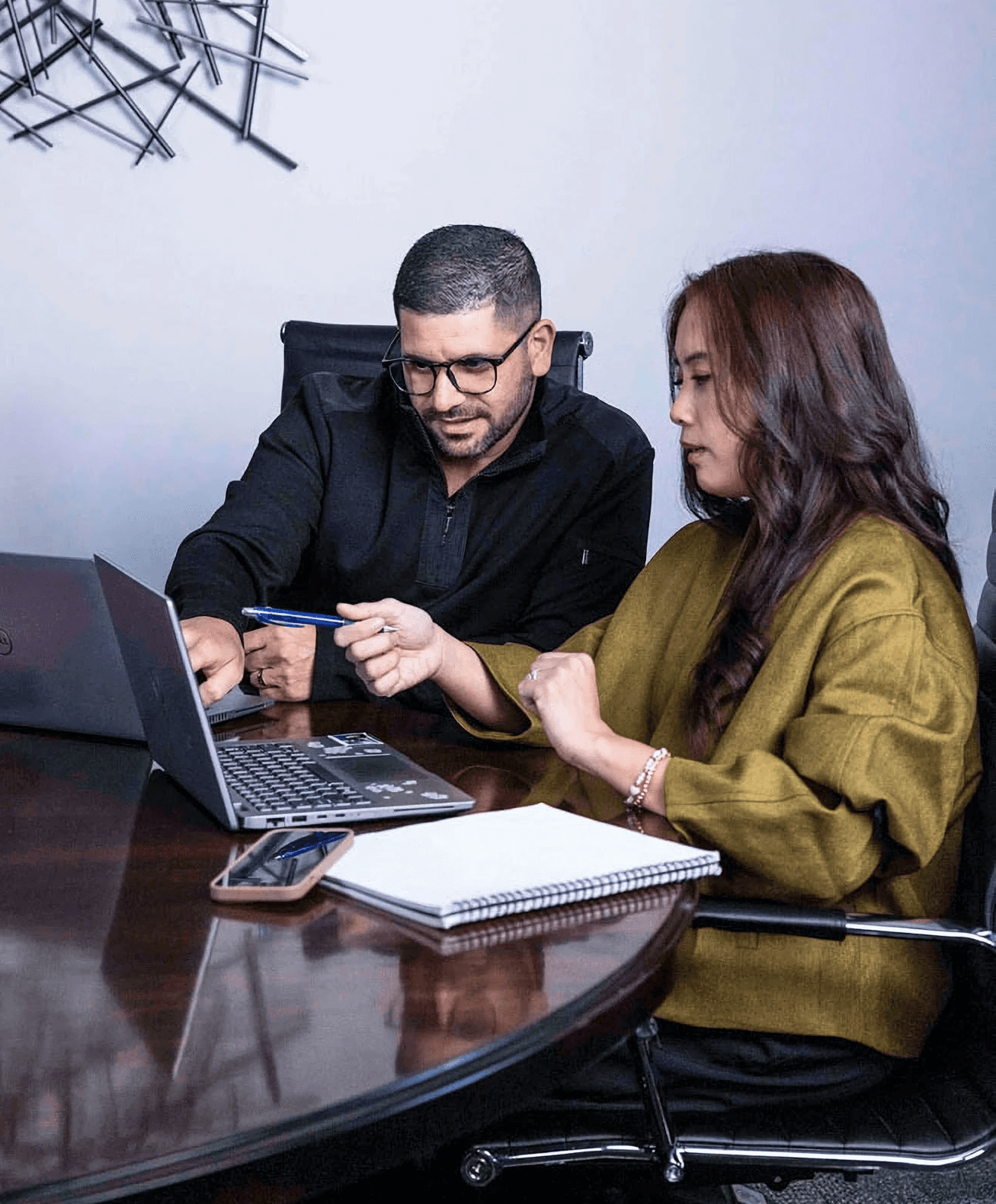 Two business professionals collaborating at a office table while reviewing data on a laptop.