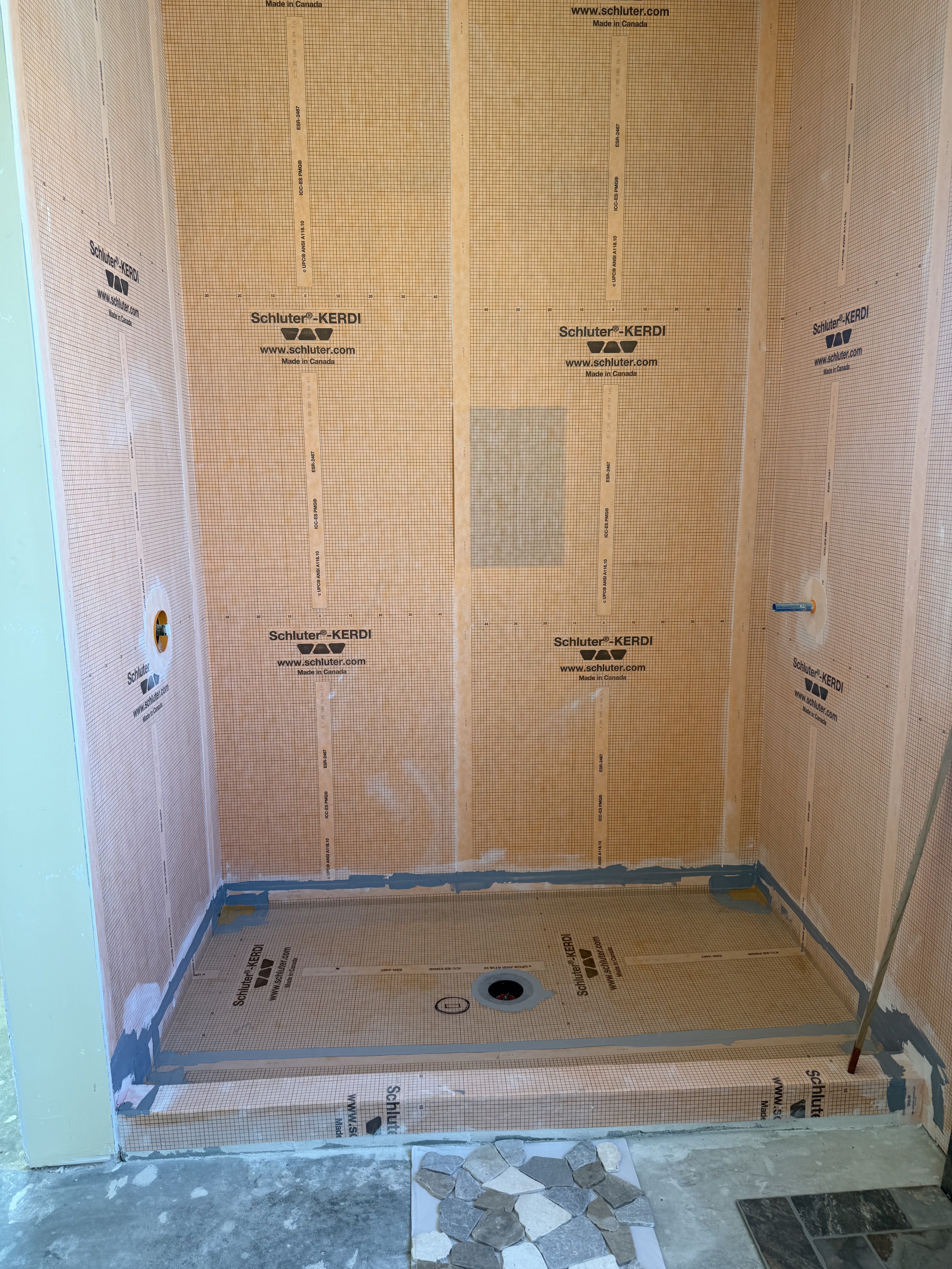 Close-up of a shower niche featuring a vibrant blue and black shattered glass or pebble mosaic tile insert, framed by light beige natural stone wall tiles.