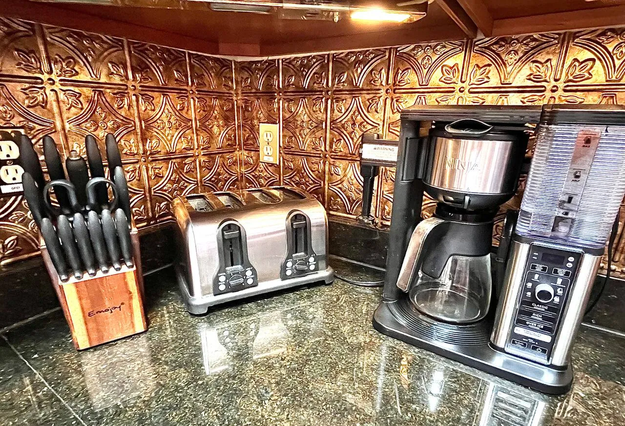 Coffee maker, toaster and knife block on granite counter with copper backsplash at Repeat Retreat