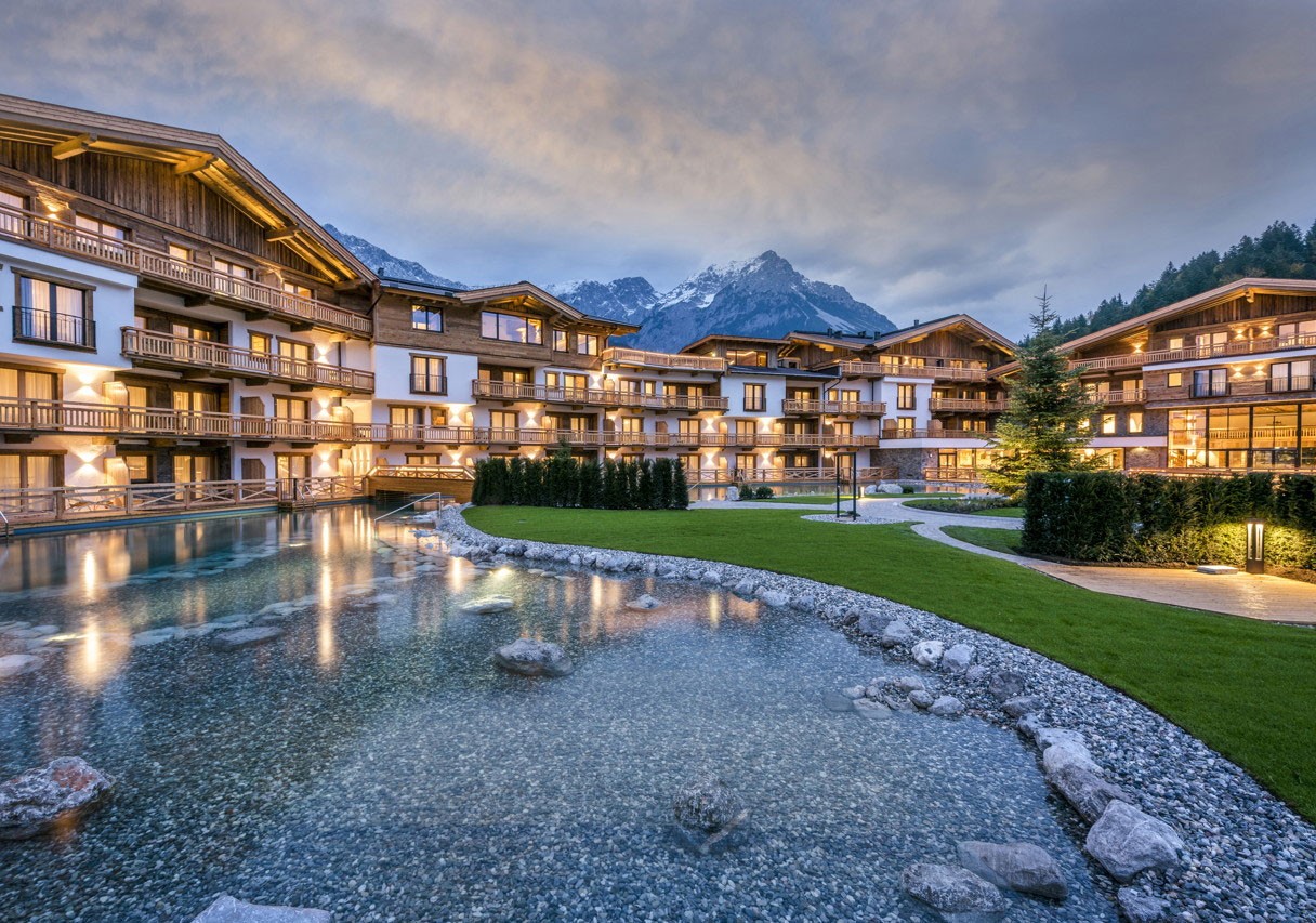 Außenfassade & Pool der Kaiserlodge Ellmau mit Blick auf das Dorf und Berge.