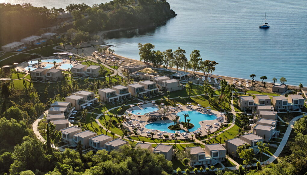 Luftaufnahme eines weitläufigen Luxus-Resorts an einer Meeresbucht mit modernen Bungalows, zwei großen blauen Außenpools und direktem Zugang zum Sandstrand.