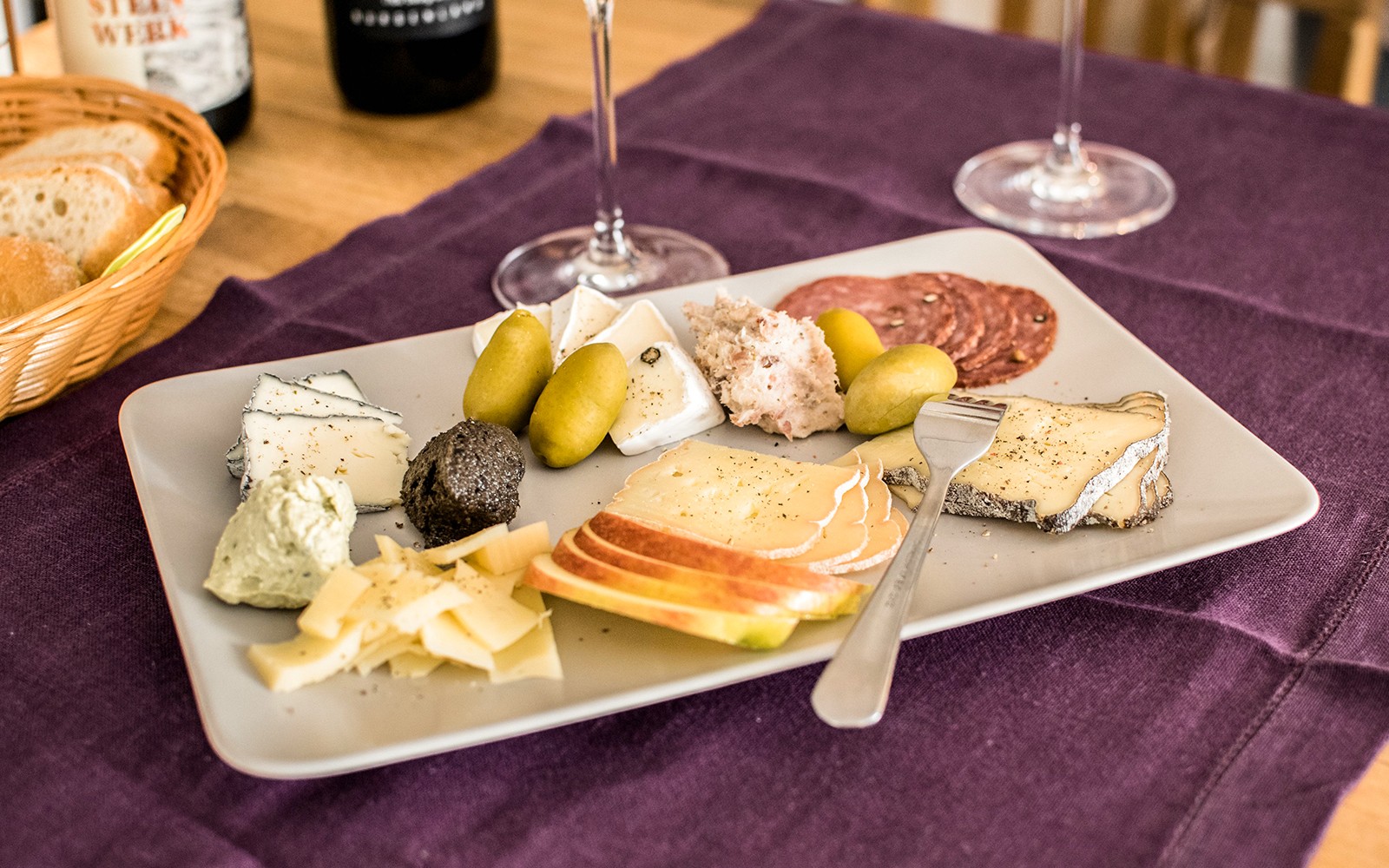 Cheese platter with assorted cheeses, olives, and charcuterie on a table with wine glasses.
