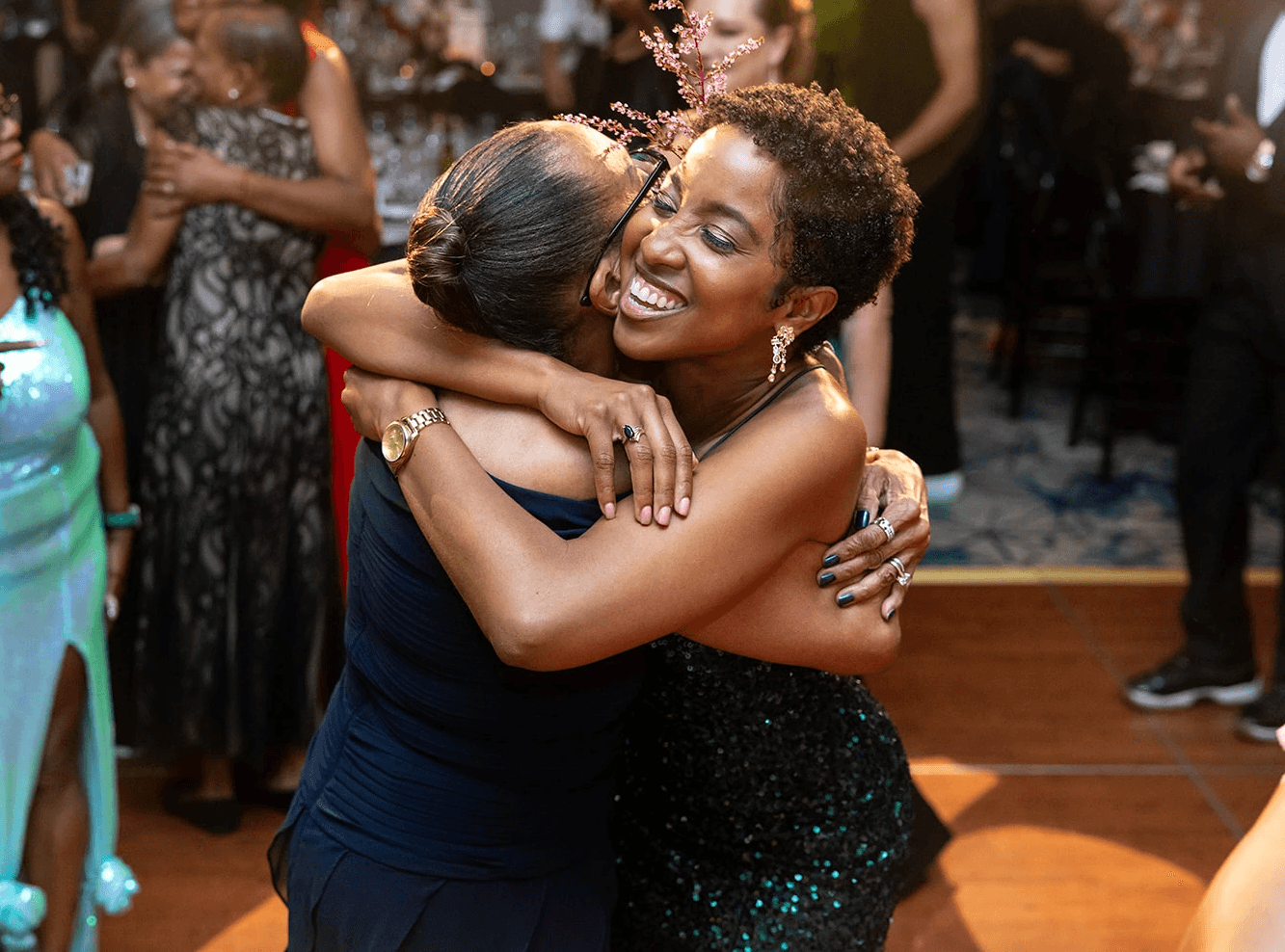 Two Black women embrace on a dance floor, looking exuberant