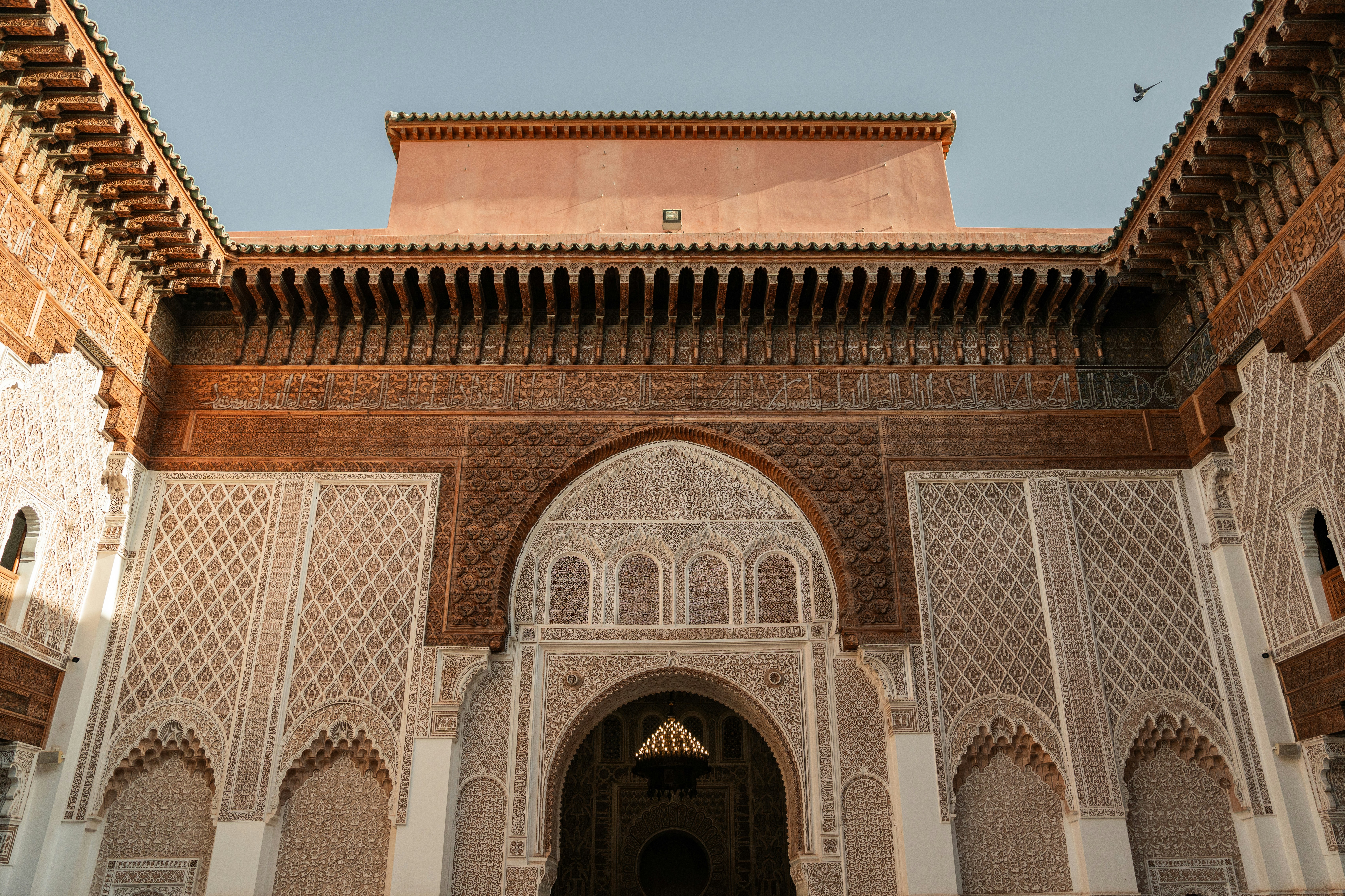 An exterior view of a traditional Pakistani building, emphasizing a textured stone or brick wall, intricate patterns, and the play of sunlight on its surface.
