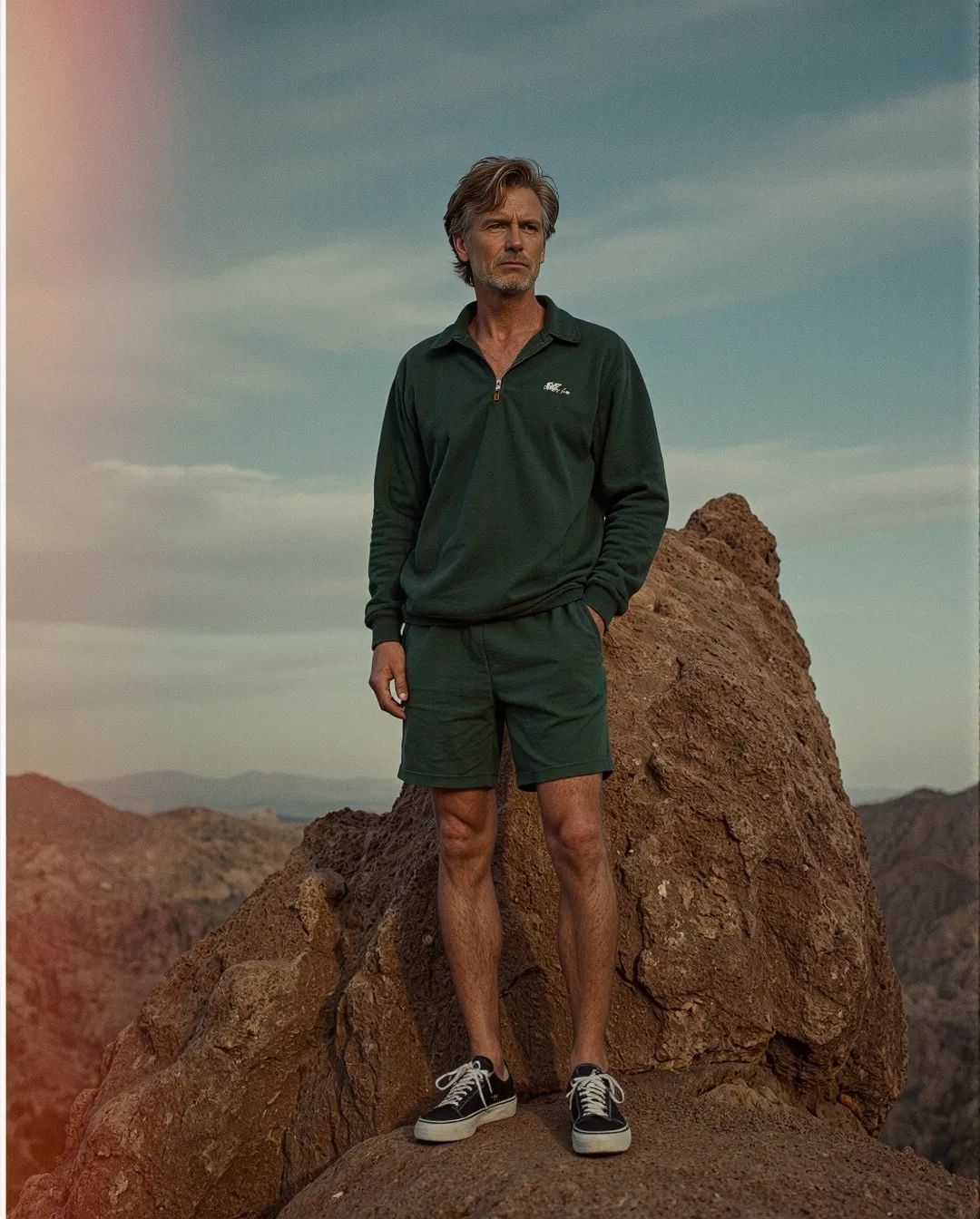 Person in green athleisure outfit standing confidently on rocky mountain peak against dramatic desert landscape and blue sky