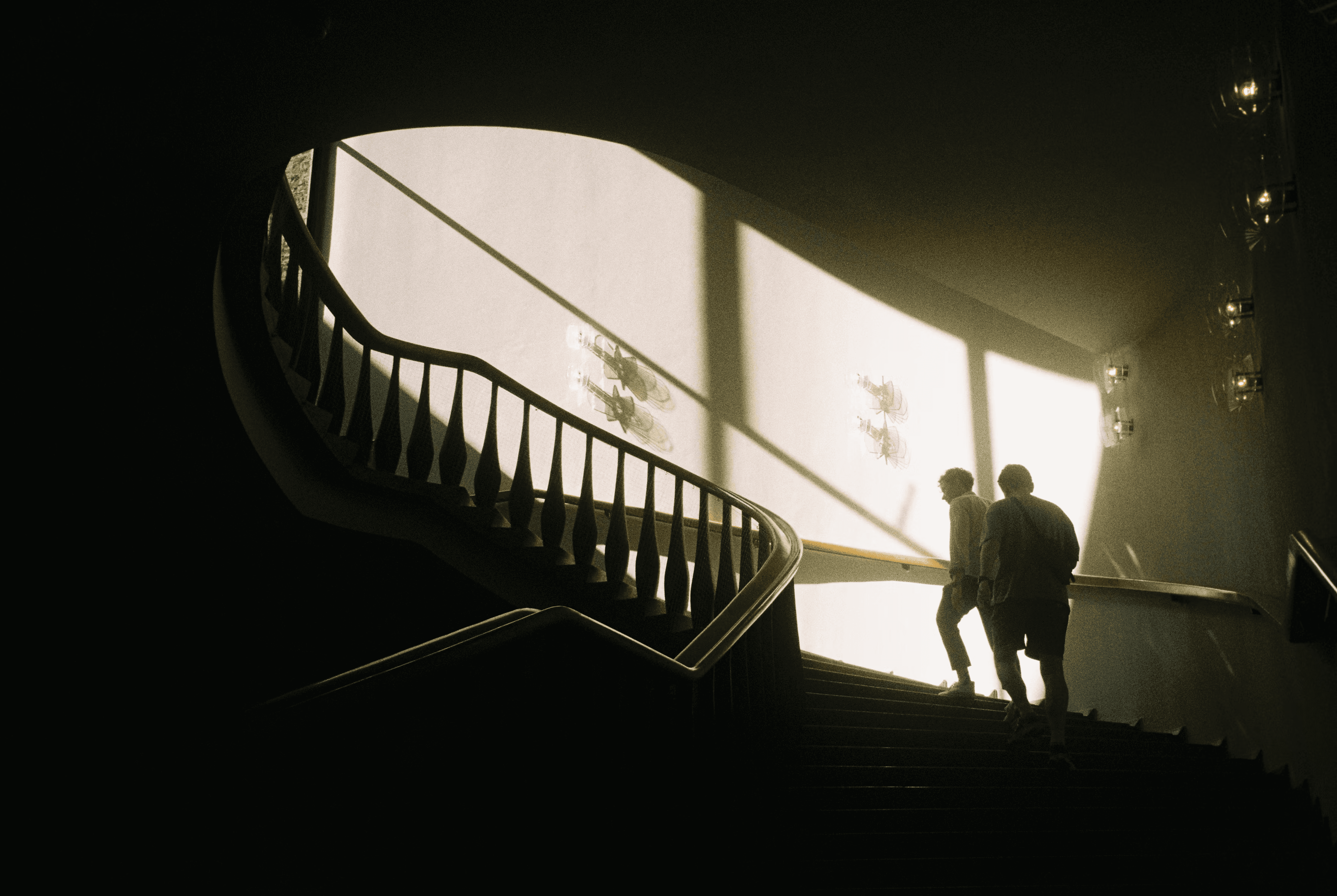 Silhouettes of two people walking up a grand, winding staircase toward a brightly lit landing, symbolizing growth and finding new paths in B2B outreach.