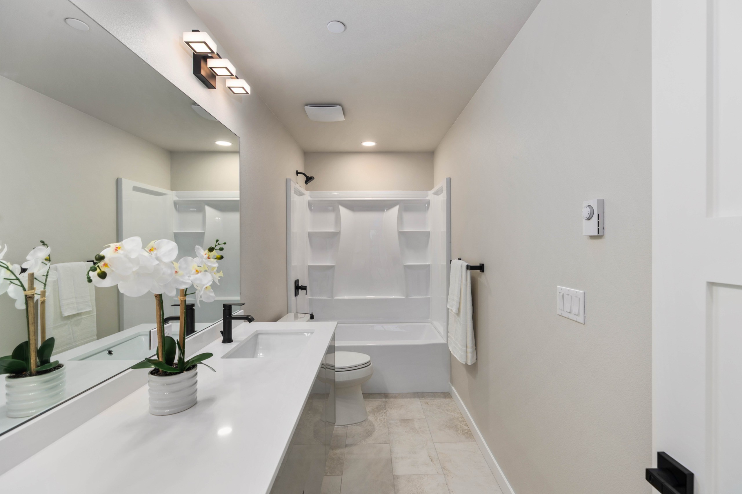 Bright luxury full bathroom with double sink white quartz vanity, black matte faucets, large mirror, soaker tub-shower combo, and marble-effect tile flooring