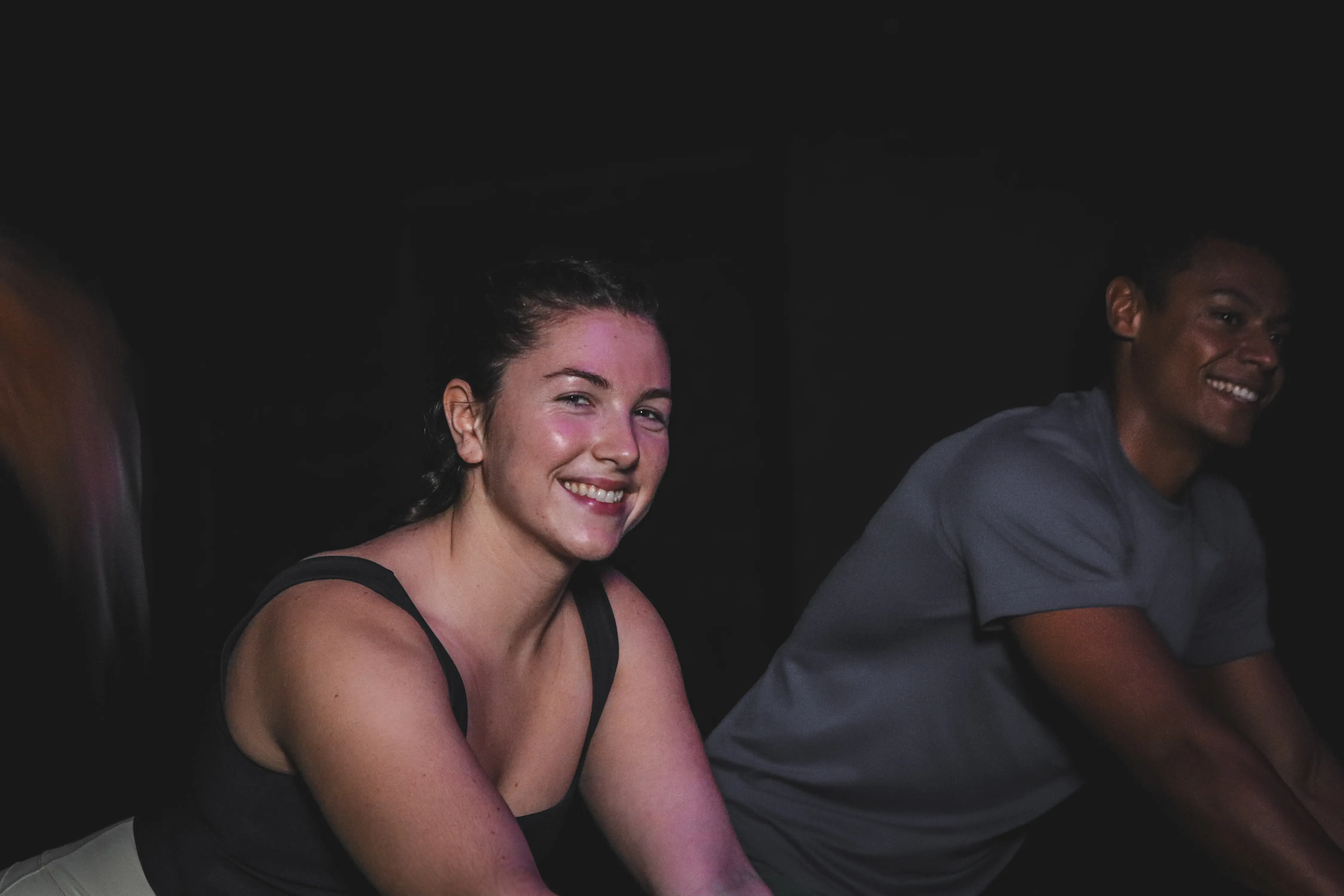 Deux participantes souriantes pendant un cours de cycling en salle sombre