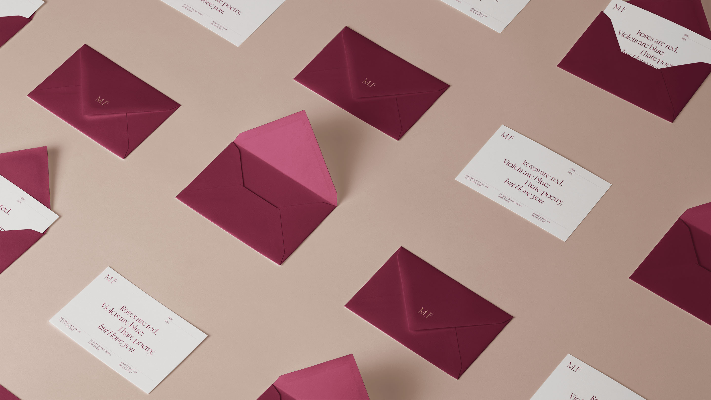 Burgundy envelopes with Mirabili Fiori monogram scattered on neutral surface with notecards