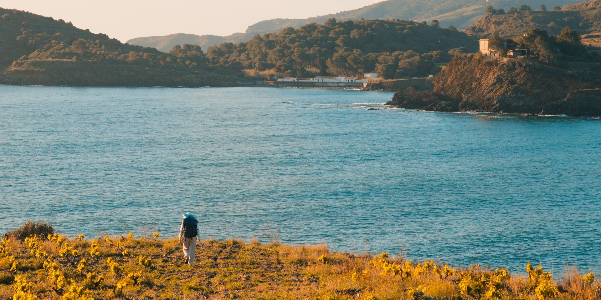 Personne en randonnée sur un sentier côtier avec vue sur la mer et les montagnes.