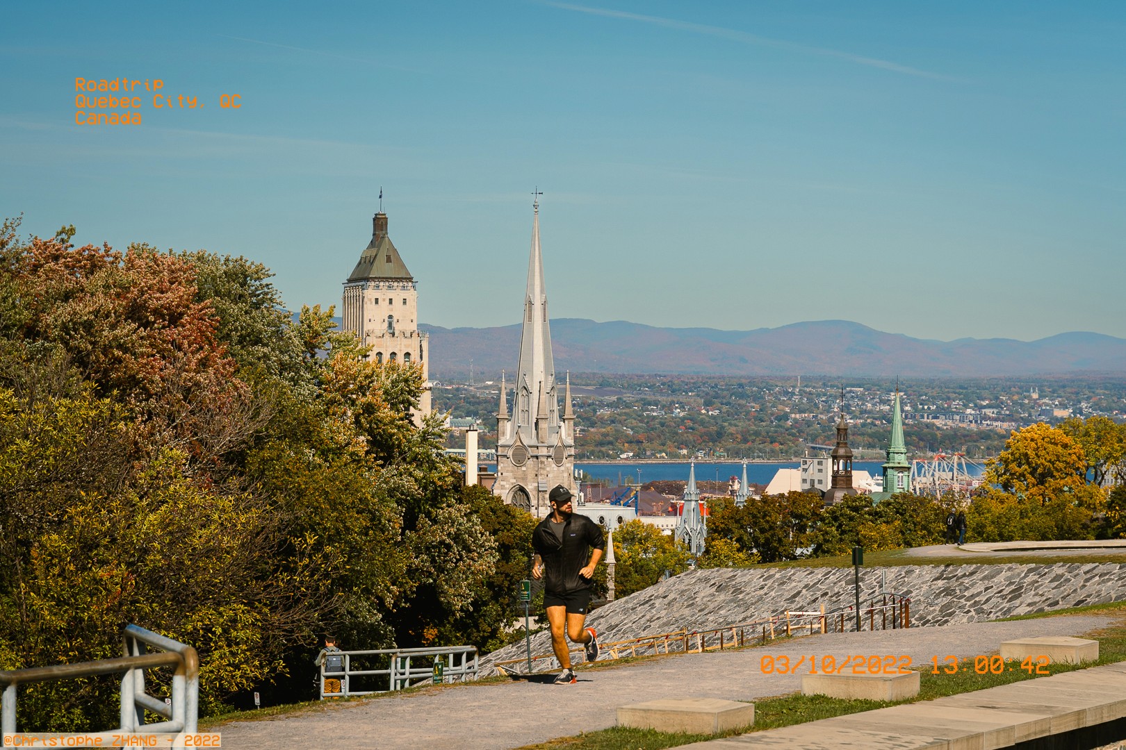 Paysage de Québec avec des bâtiments historiques et un homme courant sur un chemin surélevé.