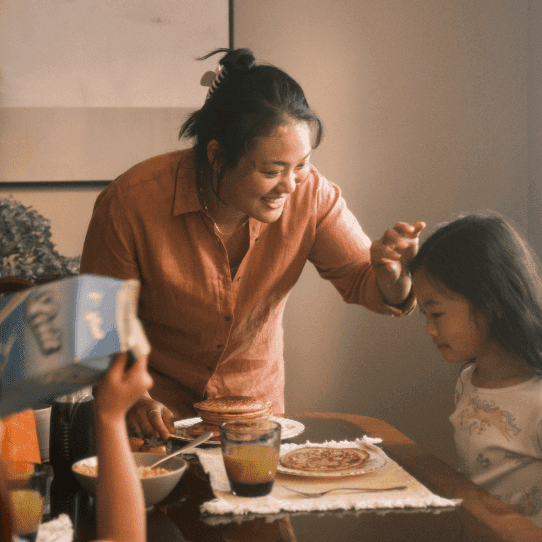 A man and a woman sit on the floor laughing while eating pizza.