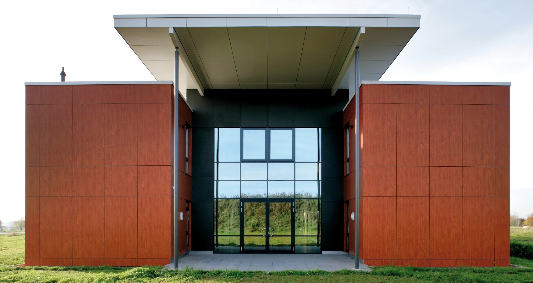 Moderne Architektur: Gebäudefassade aus braunen Holzpaneelen mit großem Glasfenster und Doppeltüren im Eingangsbereich.