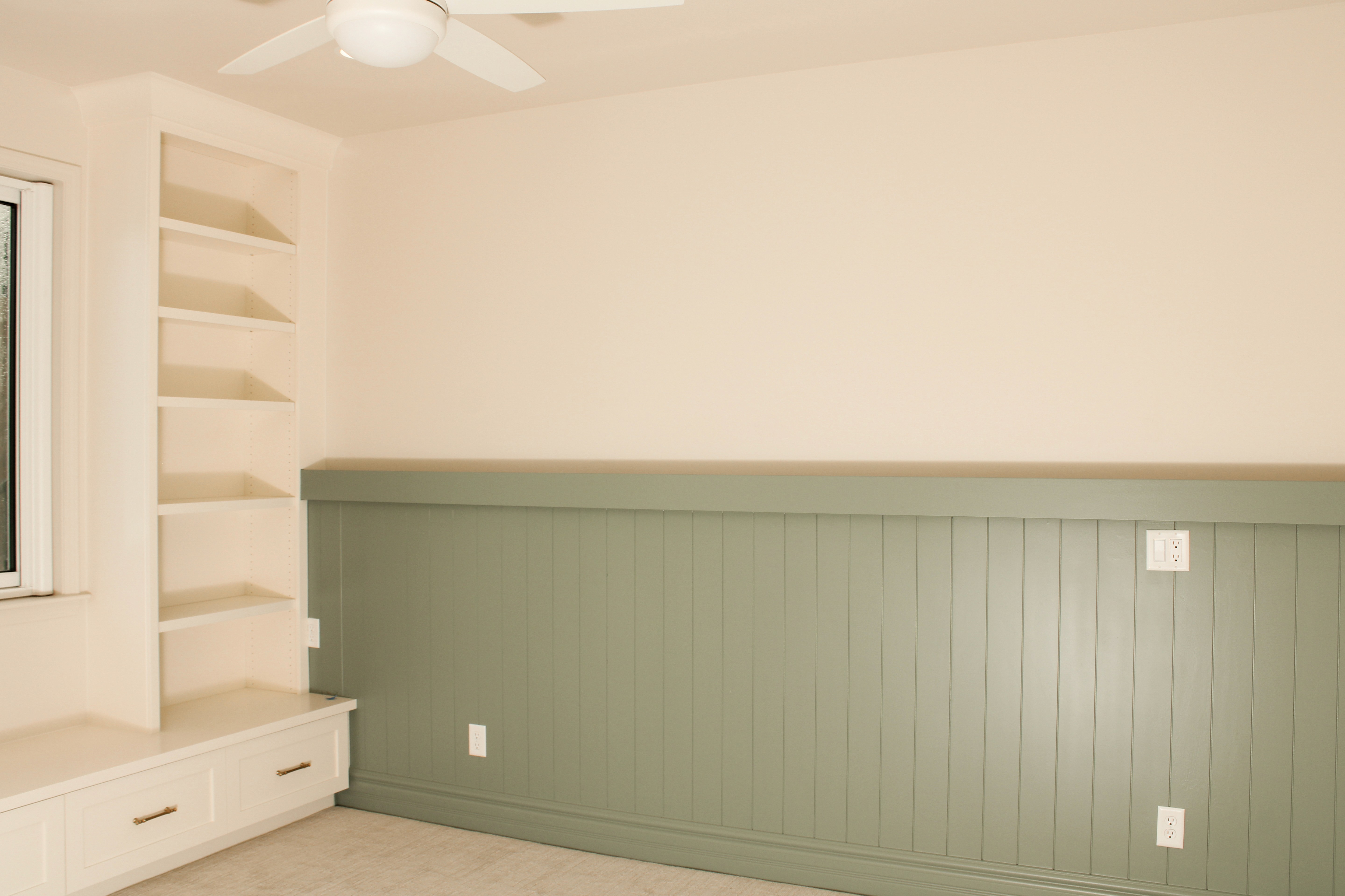 Bedroom with a neutral pain color, green accent wainscot accent, and a built in bench and shelves.