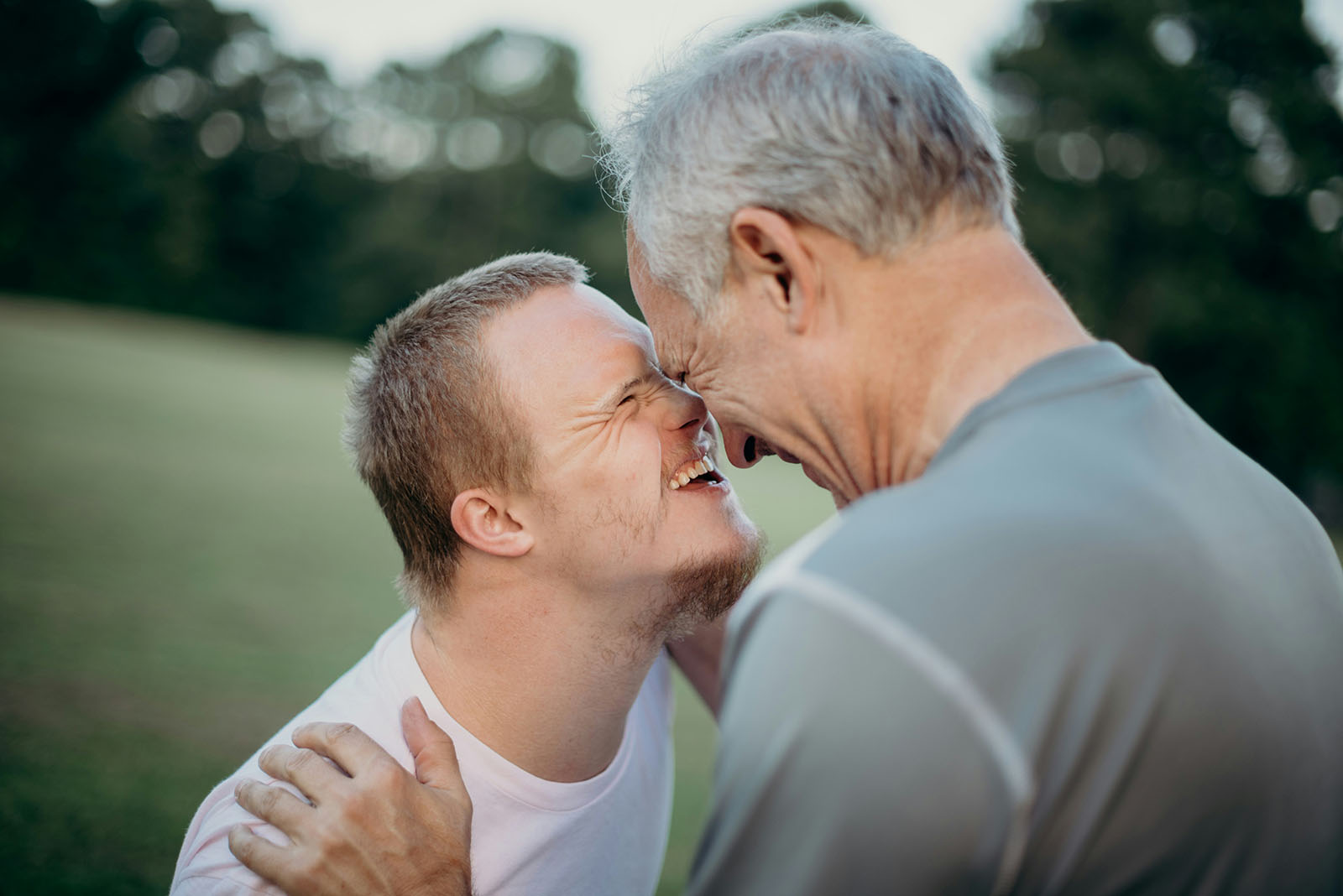 Two men smiling and touching noses outdoors.
