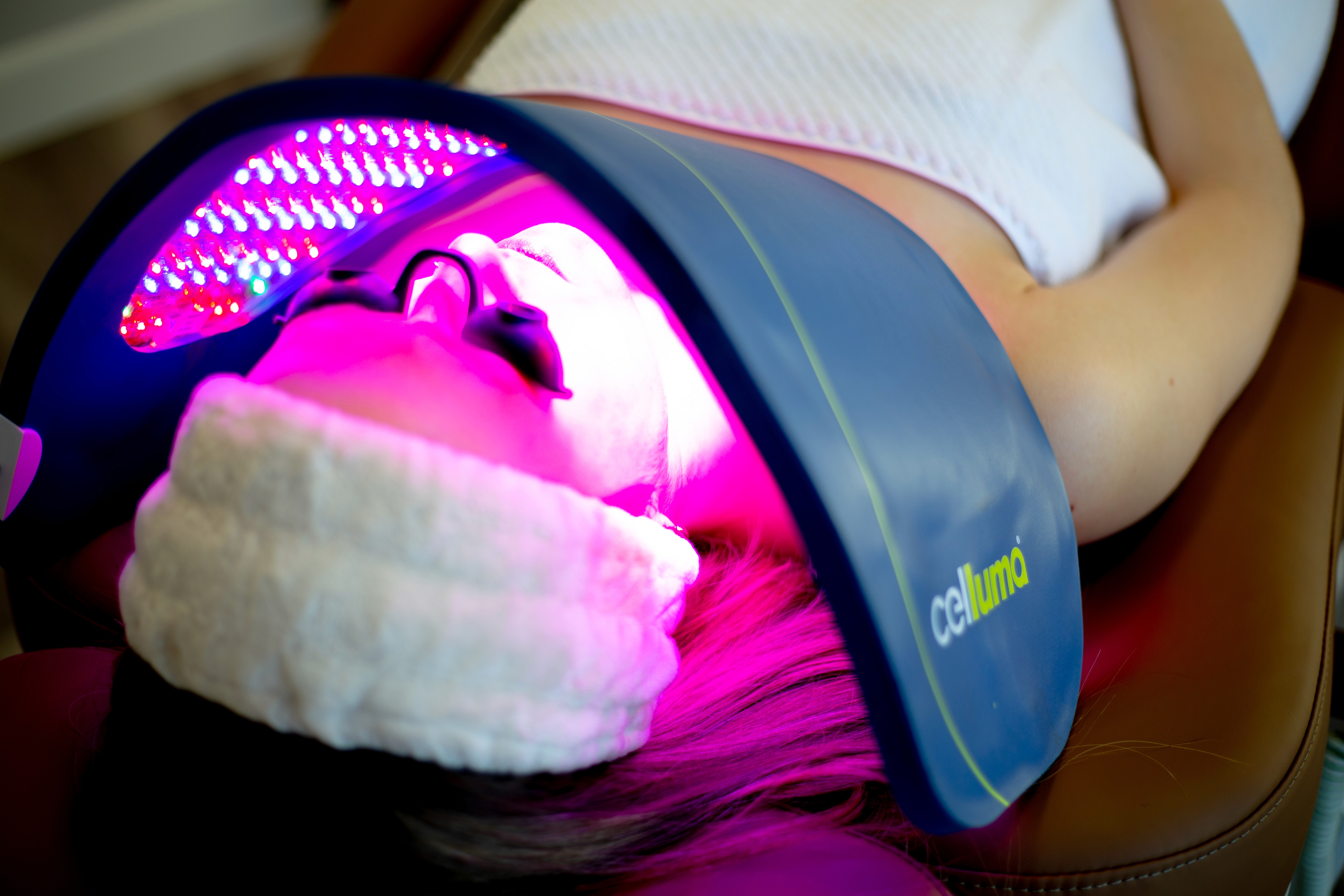 Person undergoing LED light therapy while lying down with protective goggles in a spa treatment room.