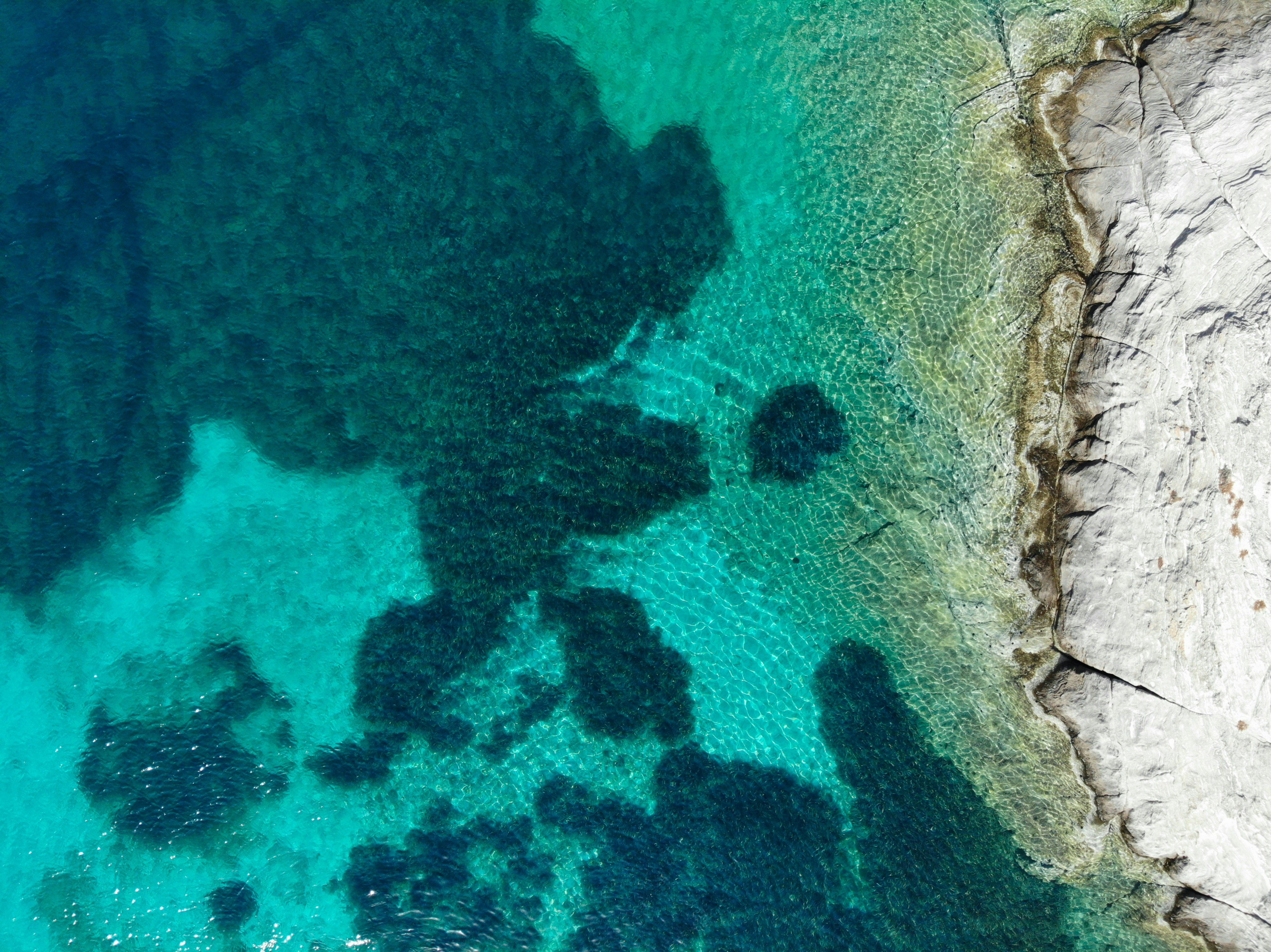 Crystal-clear turquoise sea meeting a white sandy beach with swimmers near rocky outcrops in the Aegean