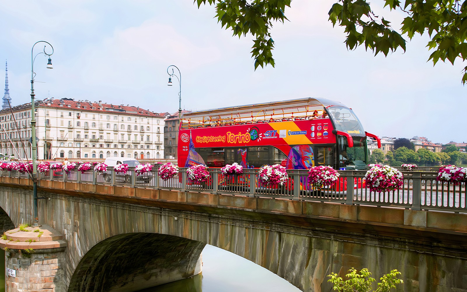 Turin hop-on hop-off bus crossing a bridge with cityscape in the background.