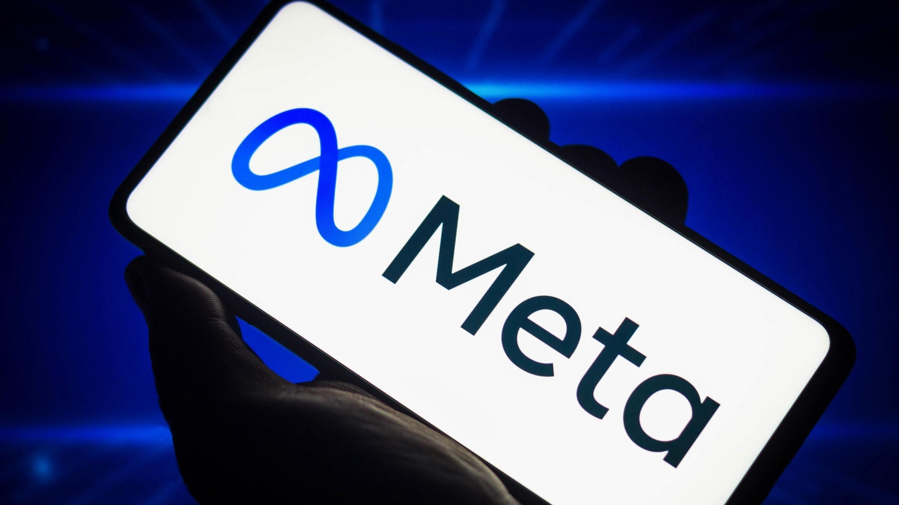 Meta logo displayed on a mobile screen held by a hand, set against a blue-colored background.