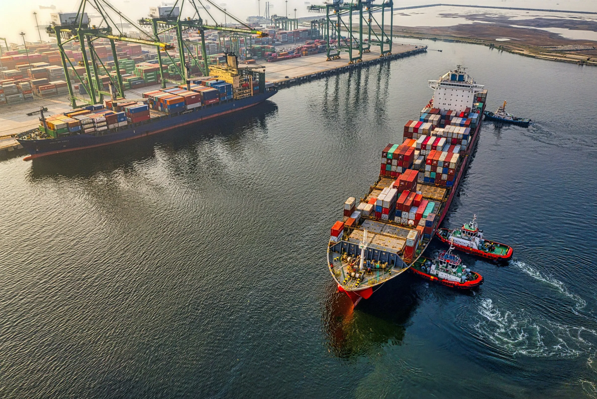 Container ship leaving a port with tugboats