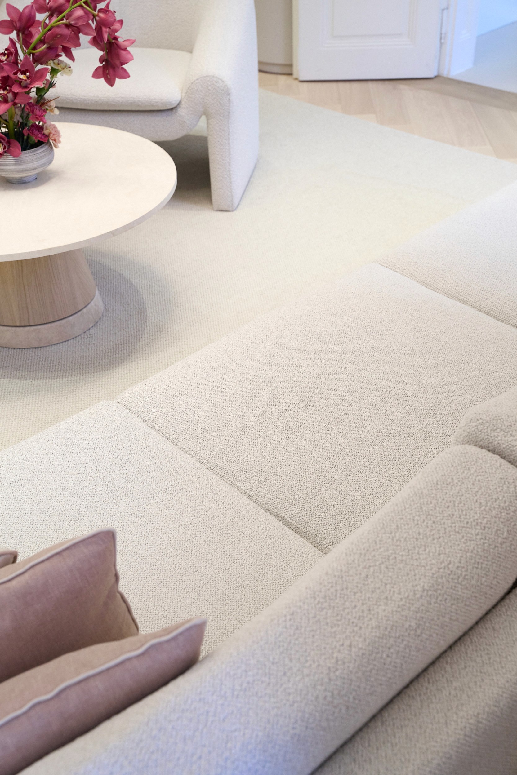 Gemütliches Wohnzimmer mit cremefarbener Couch, weißem Tisch und Blumen.